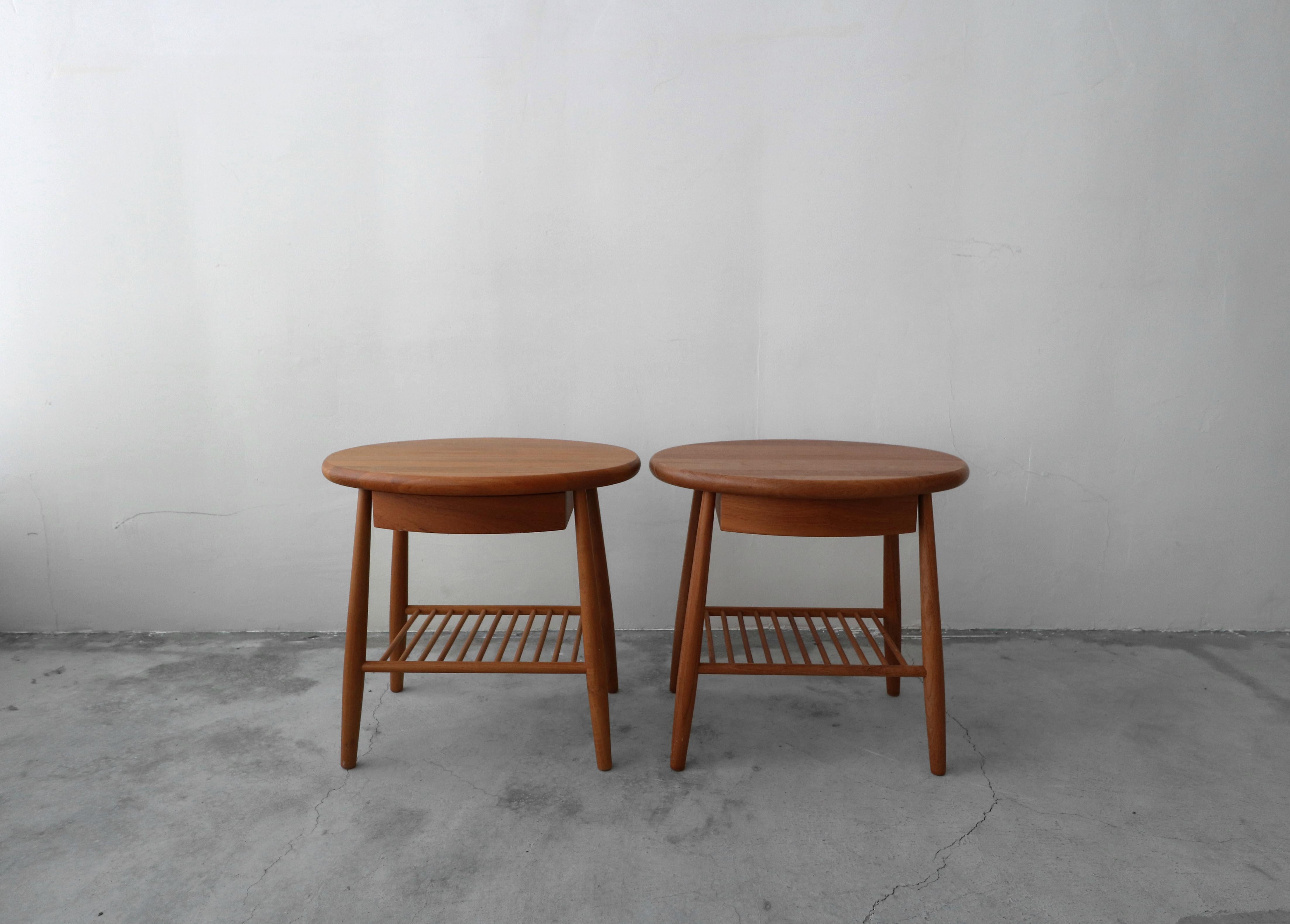 Pair of midcentury Danish tiered side tables. Sophisticated and simple, their sleek design has the perfect Danish details. Each table is constructed of solid teak, with a unique oval shape top, doweled bottom shelf and a small drawer. Tables are in