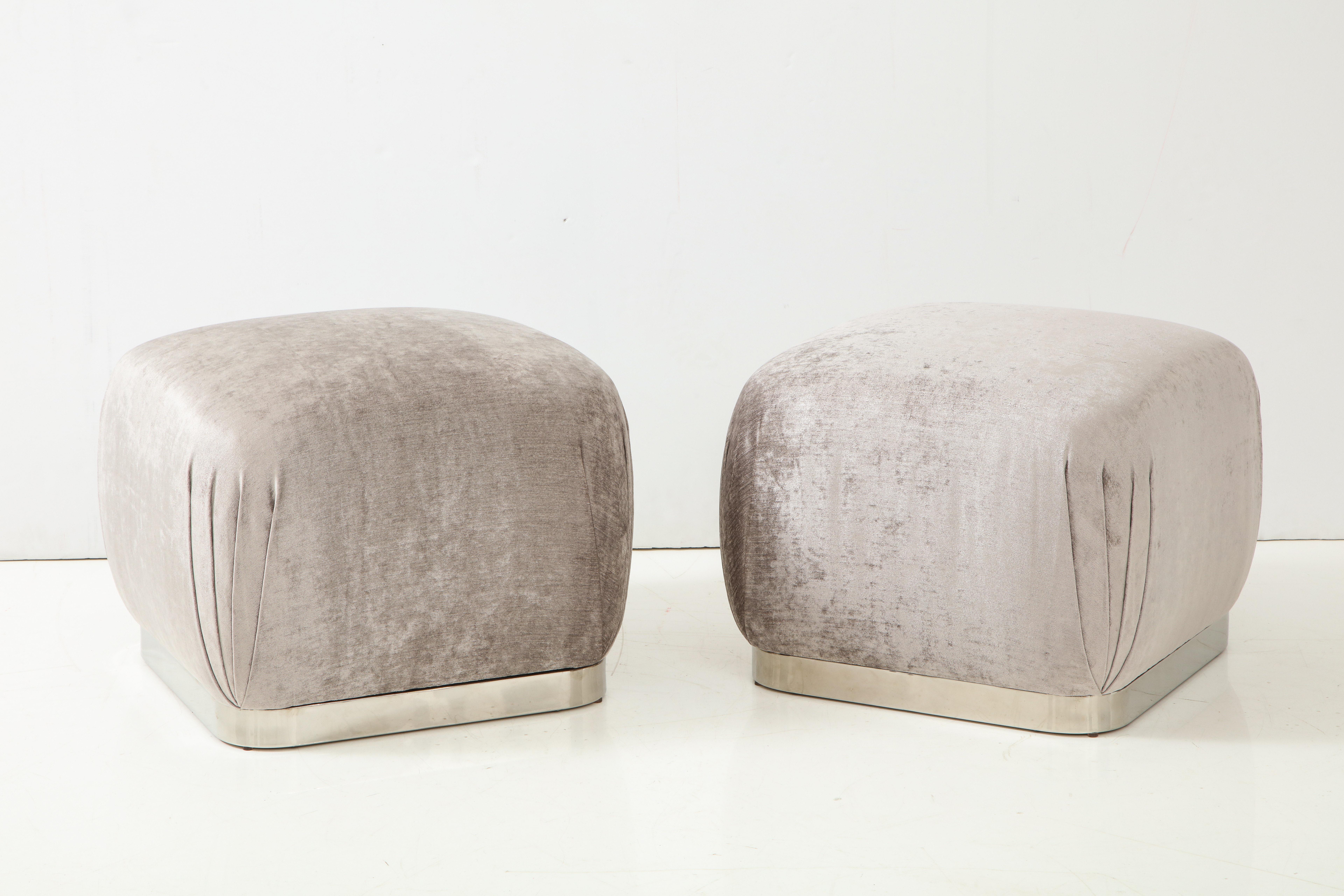 Pair of Souffle ottomans or poufs in the style of Karl Springer.
The ottomans have been newly reupholstered in a beautiful silvery grey Romo velvet fabric, and they sit on polished steel bases.