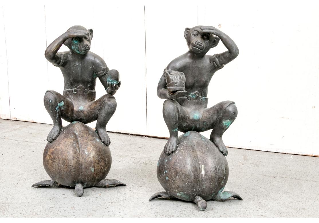 Un'affascinante coppia di scimmie sedute in bronzo che guardano in lontananza con occhi schermati mentre sono sedute su grandi pesche. Le scimmie con la coda arricciata sono vestite con perizomi con cinture decorative e indossano bracciali mentre si