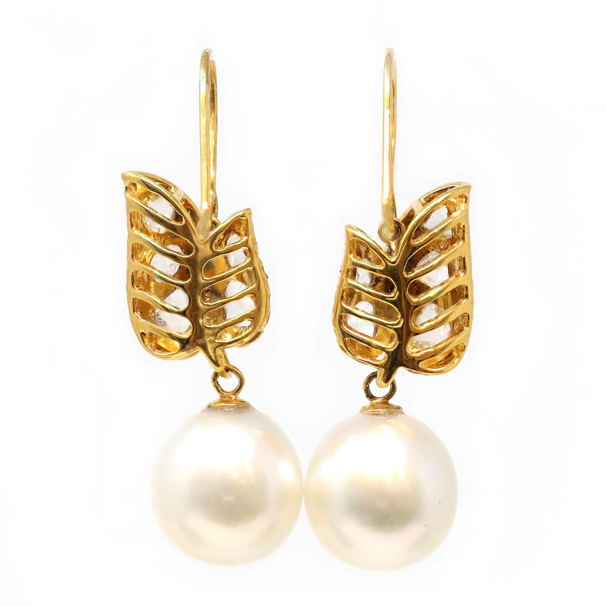 A pair of South Sea pearl and diamond dangling hook earrings in 18-karat yellow gold, circa 1990. The handmade earrings feature rose-cut diamonds with an estimated weight of 2 carats and IJ color, VS-SI clarity. The dangling white pearls measure 12