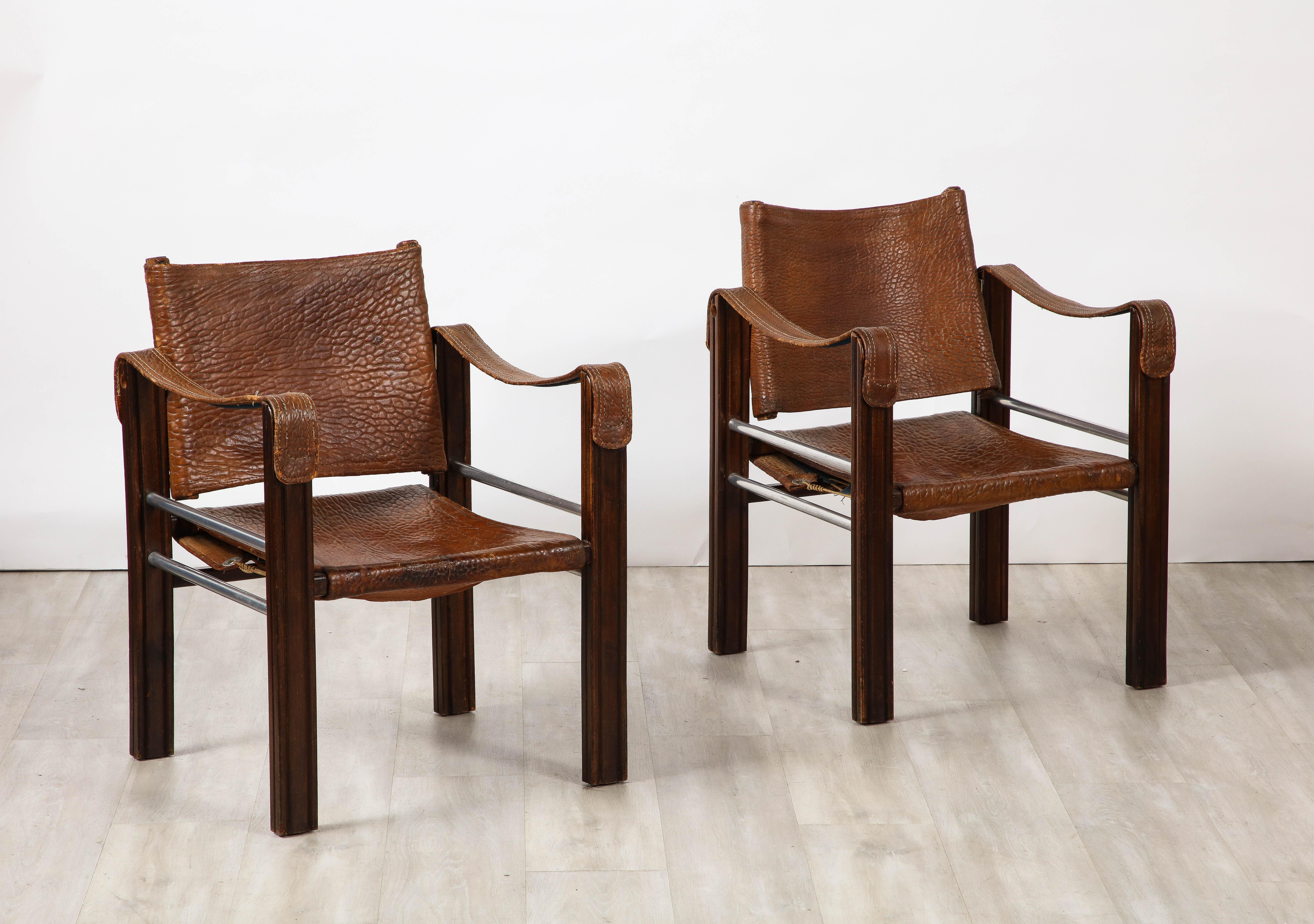 An early and unique pair of Spanish 1920's safari arm chairs in a wonderful patinated pebbled chocolate brown leather with chrome horizontal supports on the sides.  The legs are straight and are a rich carved walnut.  A beautiful contrast of the