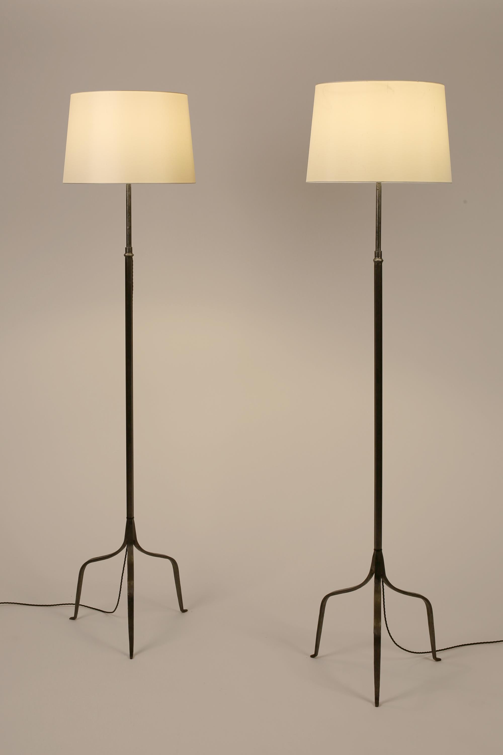A pair of fine forged iron floor lamps of simple form with slender tripod bases, in the manner of Les Artisans de Marolles. Spanish, c. 1950s. Supplied with off-white dupion silk shades.