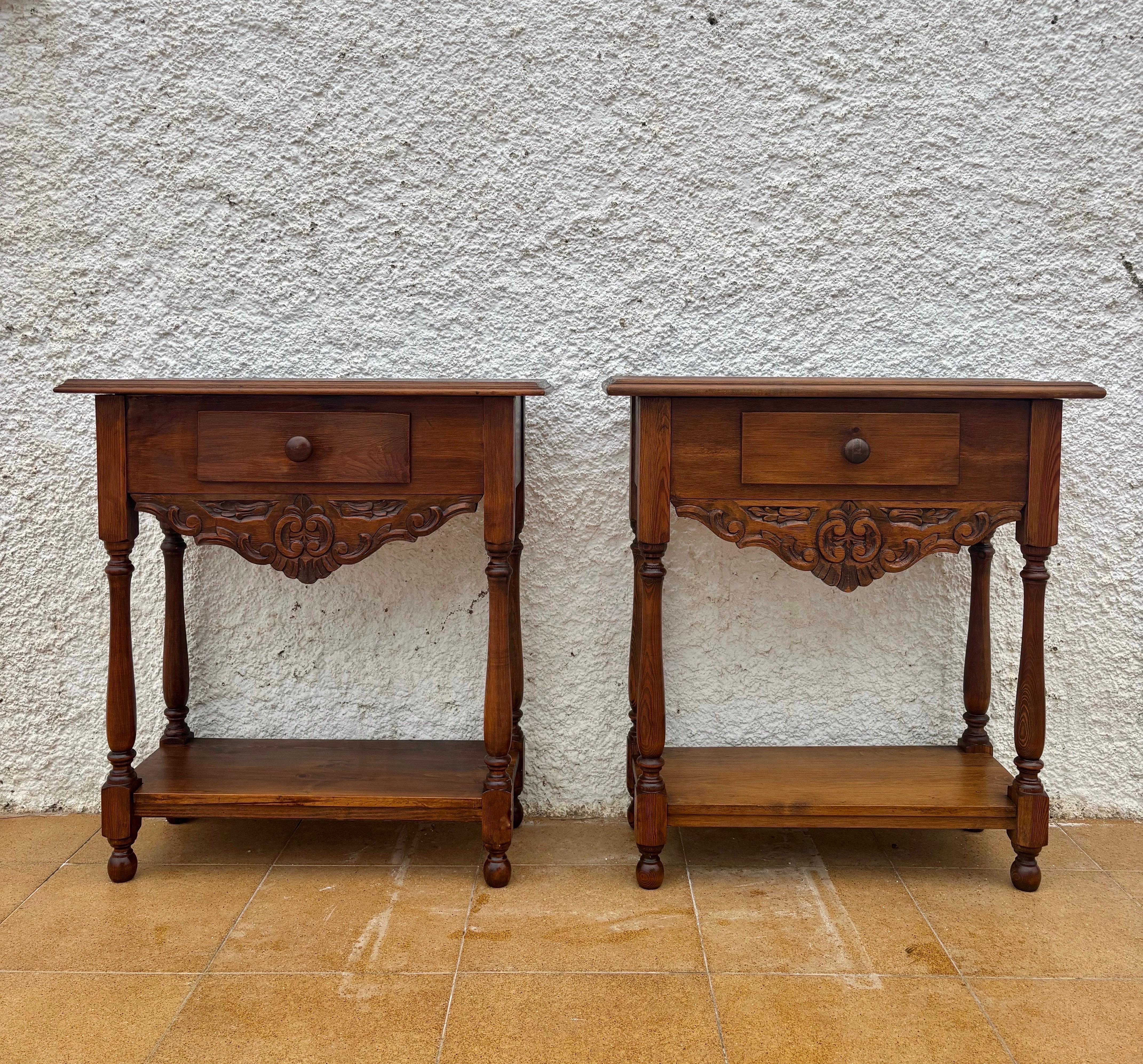 Beautiful pair of Spanish Provincial nightstands crafted in solid wood, dating from the mid-20th century. Each table features a single drawer with wooden knob and a lower open shelf for display or storage. The front is adorned with a hand-carved