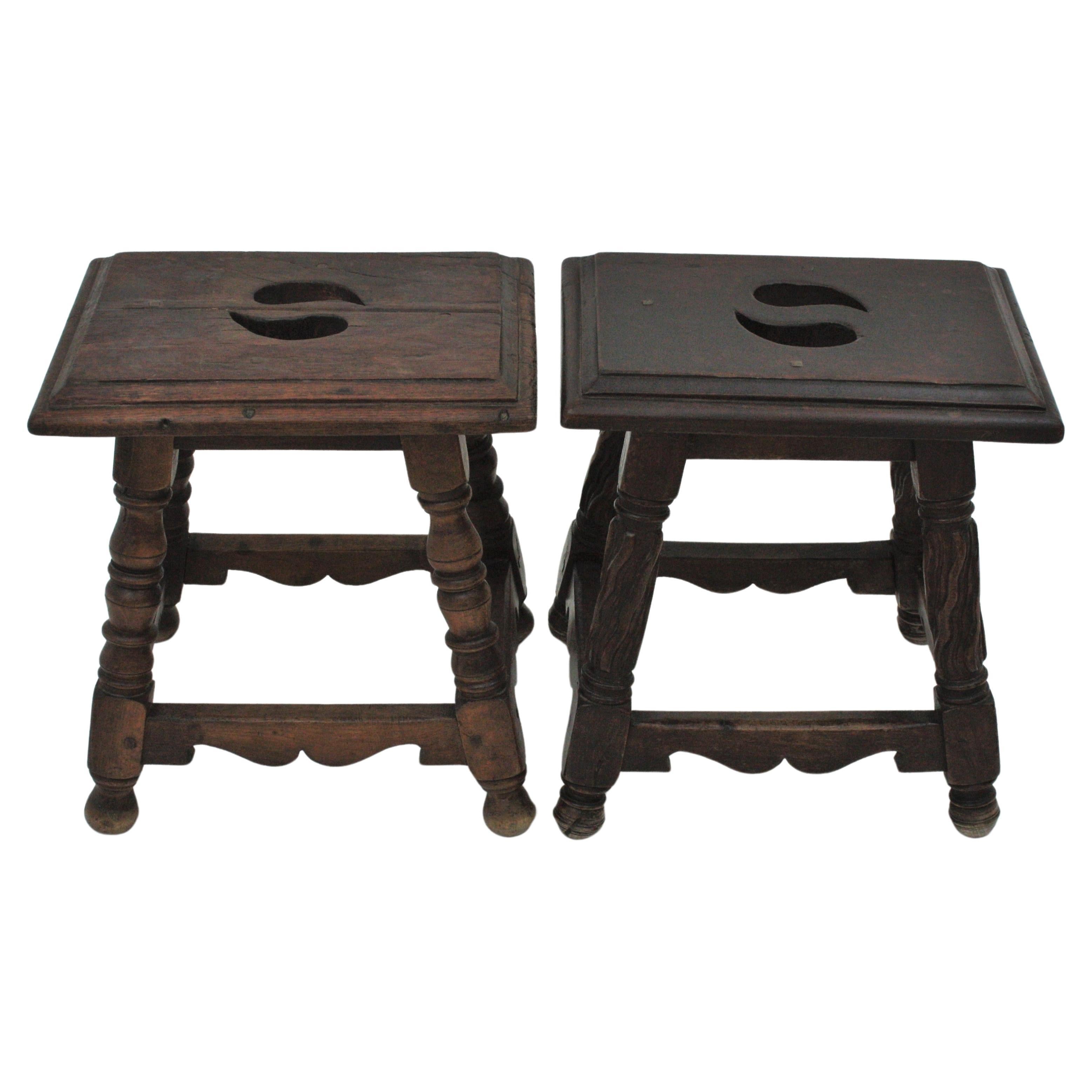 Unmatching pair of stools / side tables in walnut wood,  Spain, 1940s.
These stools feature rectangular tops supported on turned legs with different design. Both tops are adorned by tear drop shaped cut holes and wood nails. 
They are very versatile