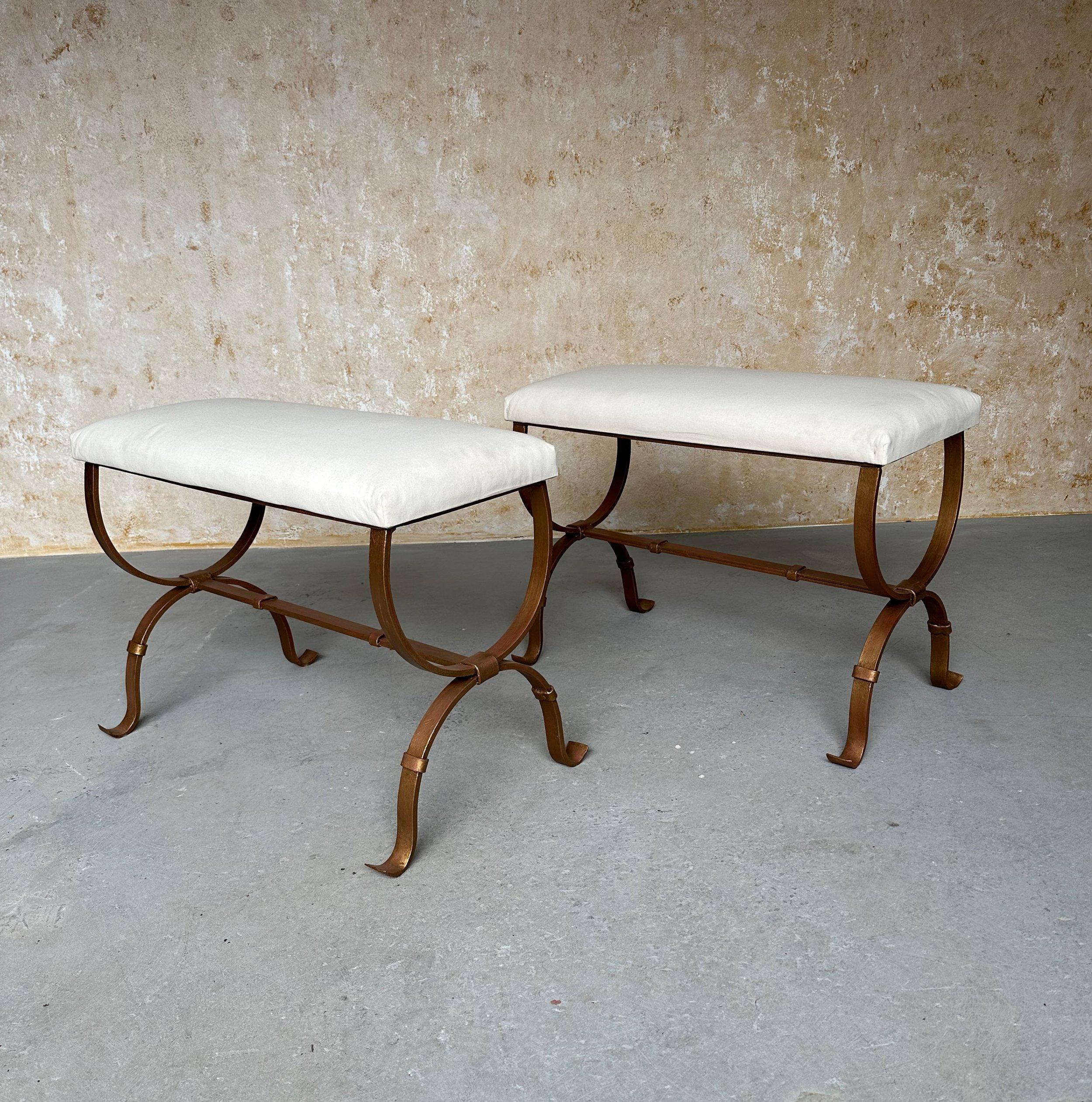 This elegant pair of Spanish gilt iron benches was recently handcrafted by expert European artisans using traditional iron-working techniques. The hand forged iron bases have central stretchers and gently curved feet with decorative band details