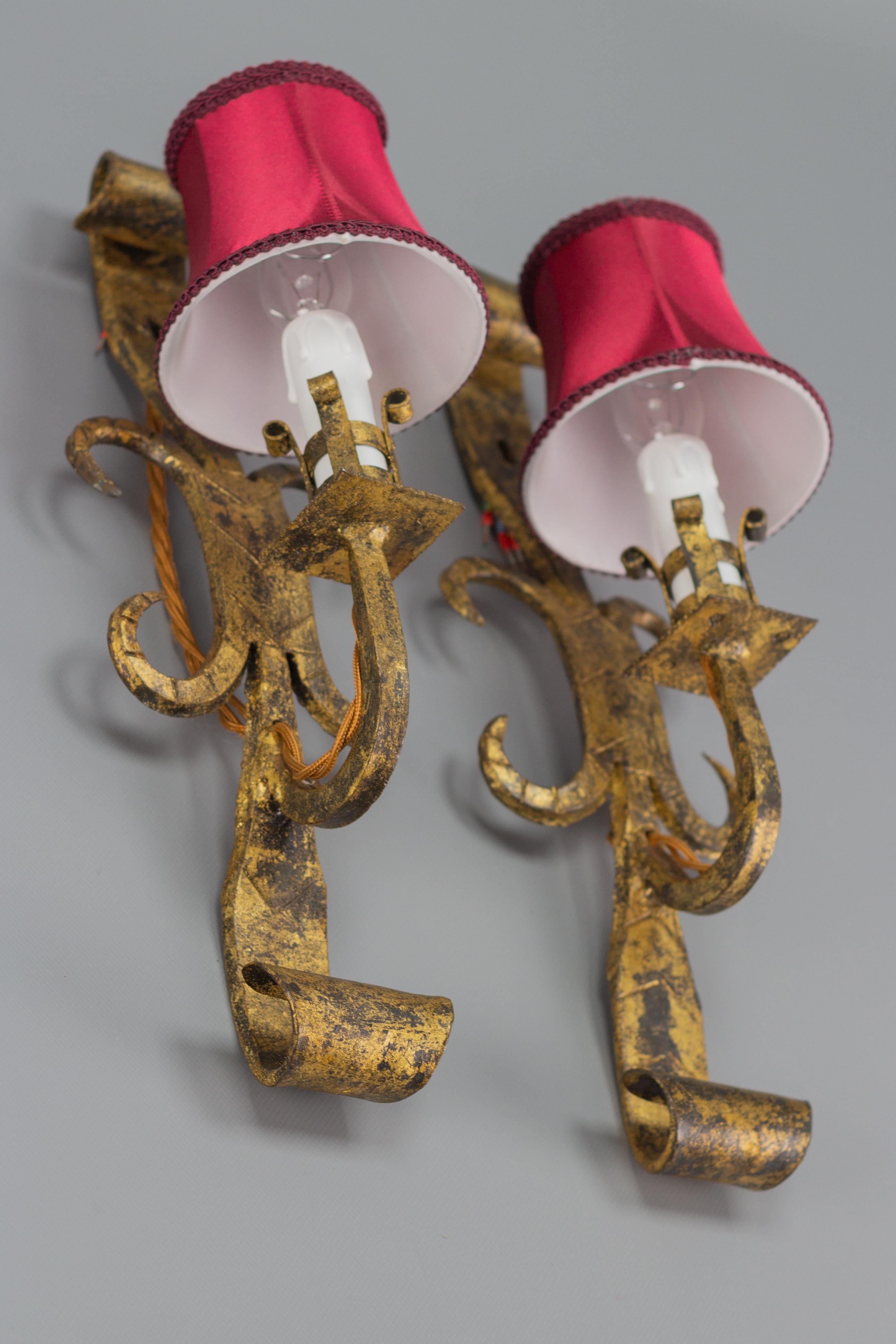 A beautiful pair of Gothic Revival style gilt-wrought iron wall sconces with red lampshades (new), Spain, 1940s.
Each wall light fixture has one socket for E14-size light bulb.
Dimensions: height: 43 cm / 16.92 in; width: 13 cm / 5.11 in; depth: 16