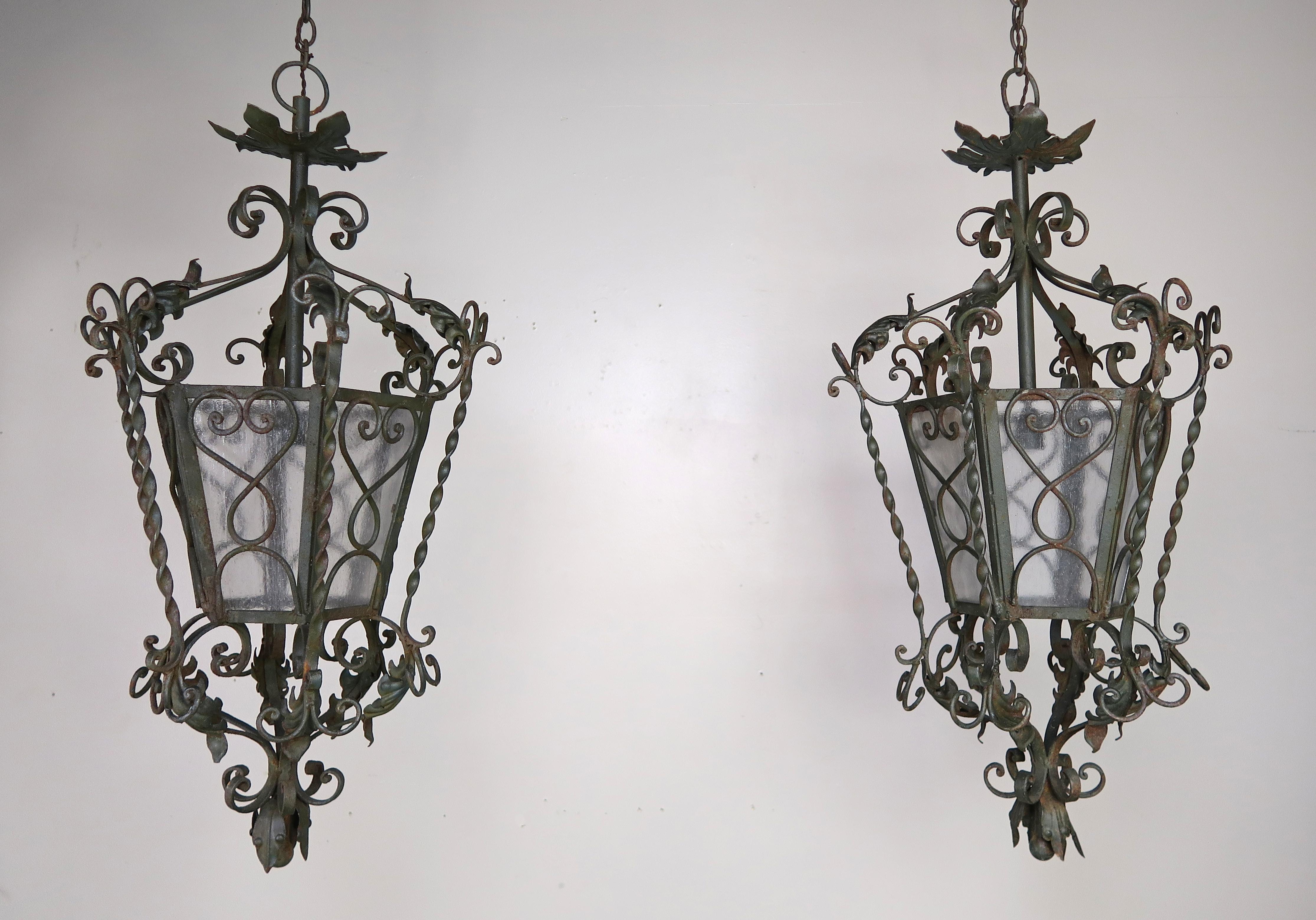 Pair of Spanish six sided handwrought iron and glass lanterns with beautiful ornate details throughout. The lanterns are both newly rewired and include chain and canopy. Ready to install.