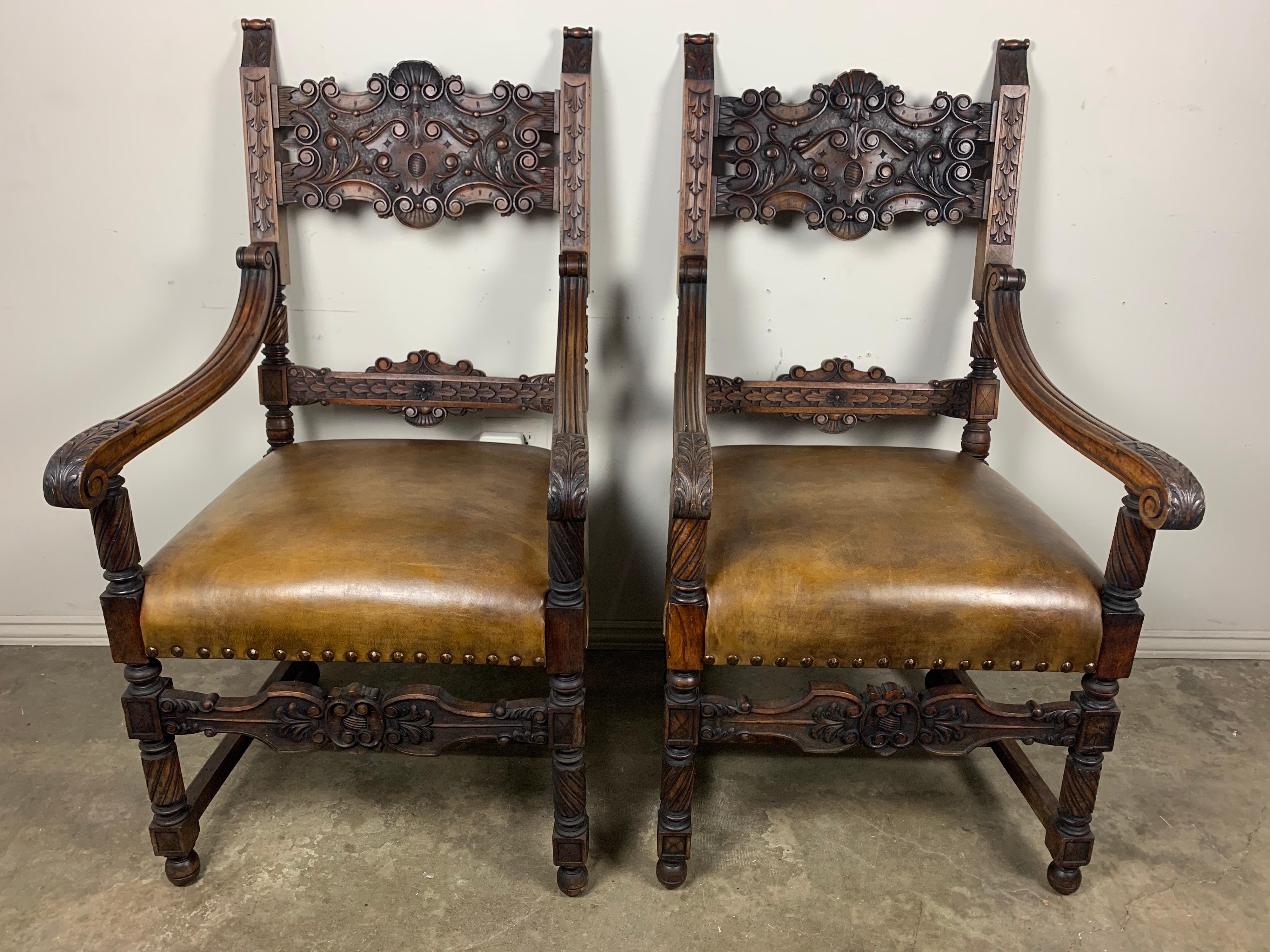 Pair of walnut carved Spanish armchairs upholstered in a chestnut brown coloration with antique brass nails.