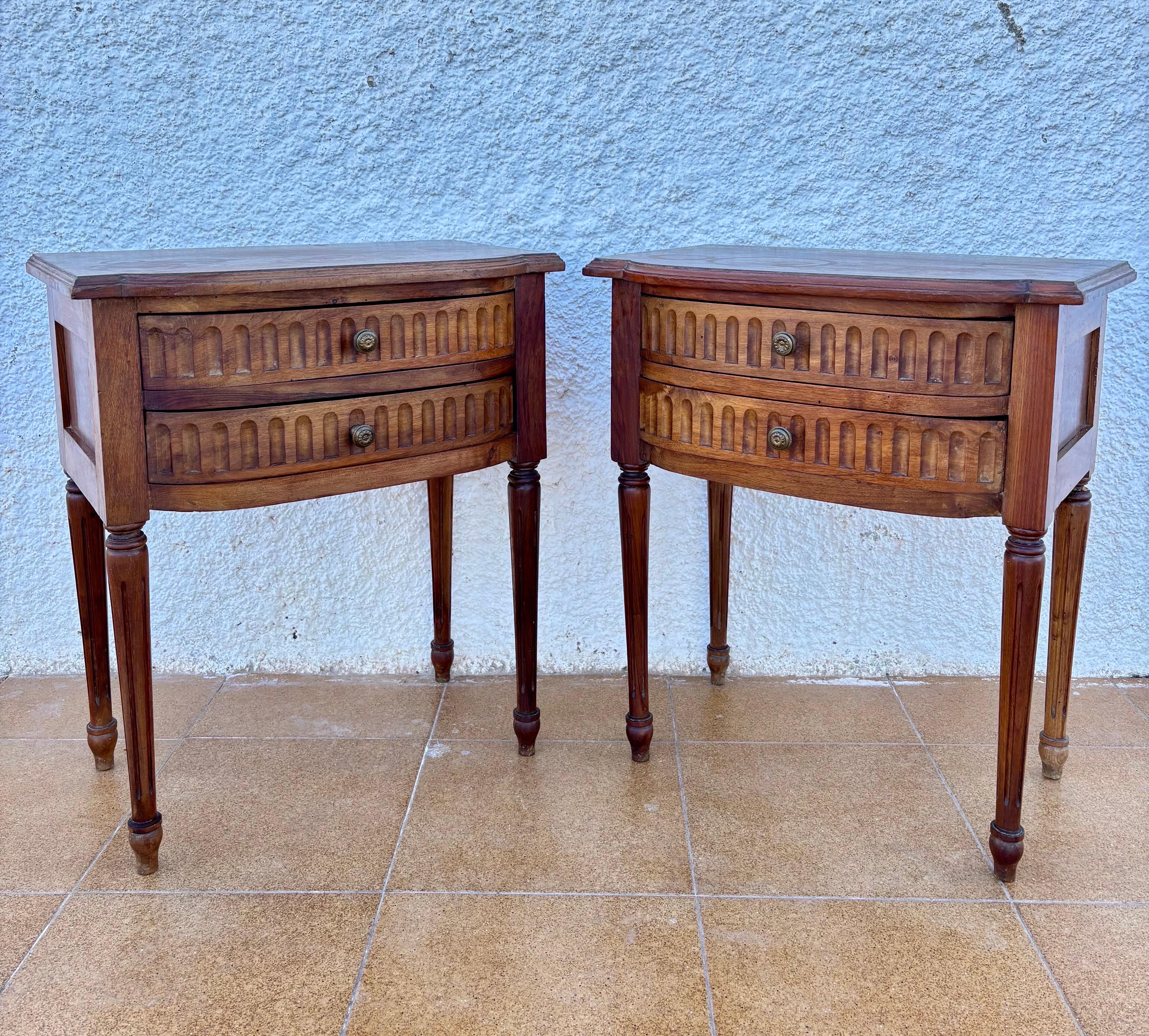 Elegant pair of Spanish neoclassical nightstands/side tables crafted in oak, dating from the early 20th century in the Louis XVI Revival style. Each piece features two curved drawers with distinctive carved vertical arches, adding rhythm, texture