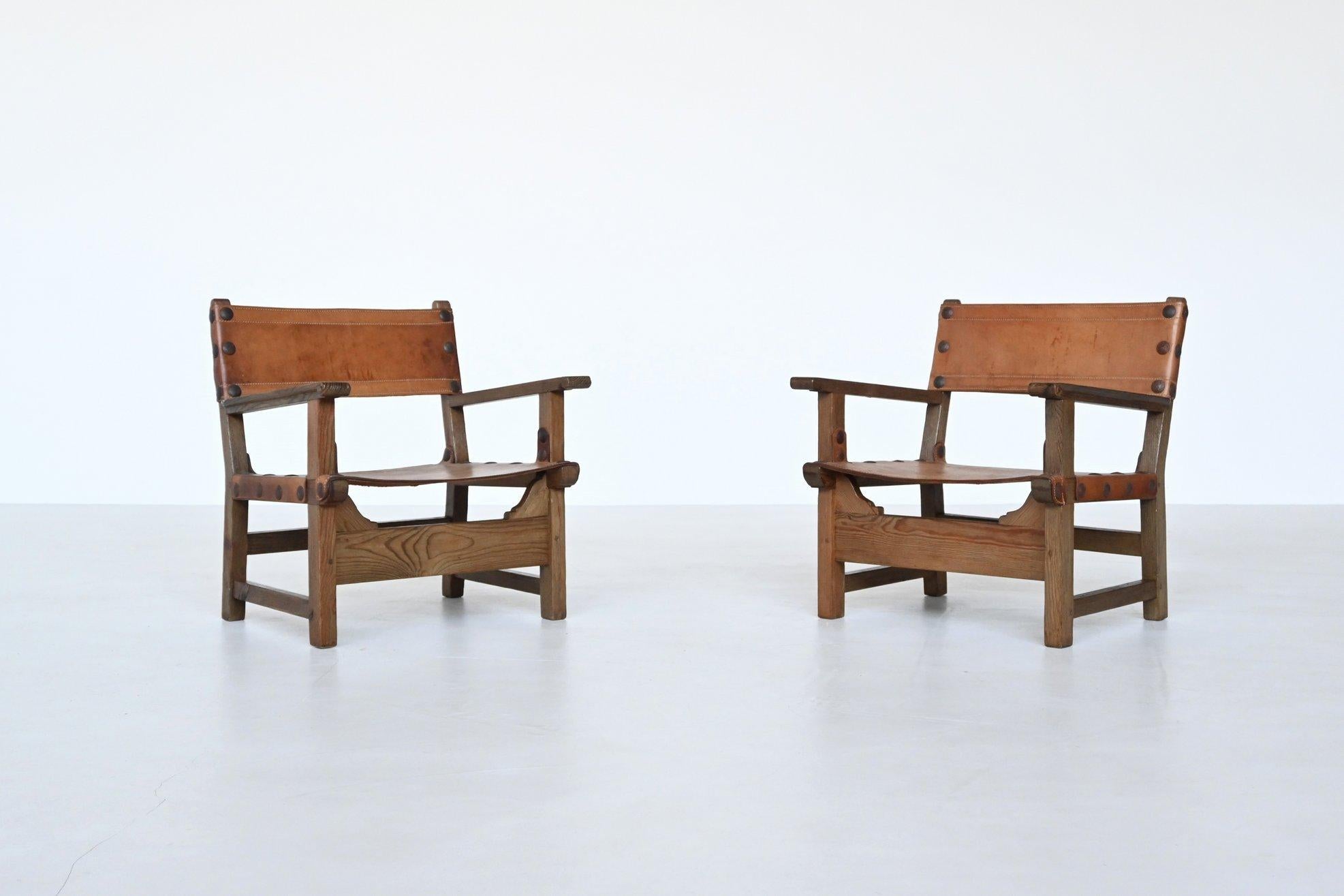 Stunning pair of “Spanish” lounge chairs by unknown designer or manufacturer, Spain 1960. These beautiful shaped chairs are made of solid oak wood with beautiful natural saddle leather. The leather is still original and has a very nice patina due