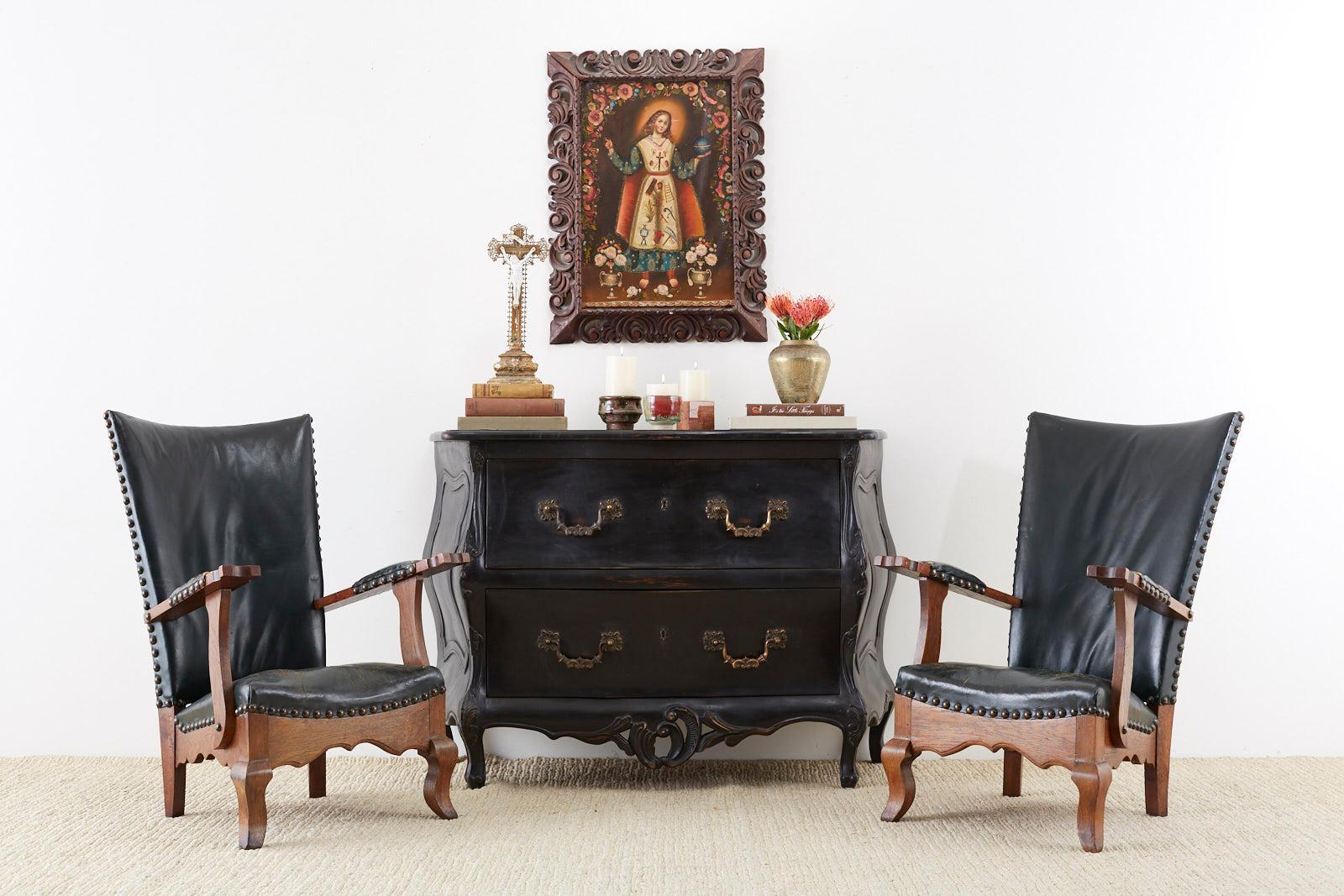 Amazing pair of Spanish colonial revival mission style arm chairs or lounge chairs. Constructed from Spanish oak and finished in a hunter green leather. The chairs have a tall, winged back and feature large brass tack nail head along the borders.