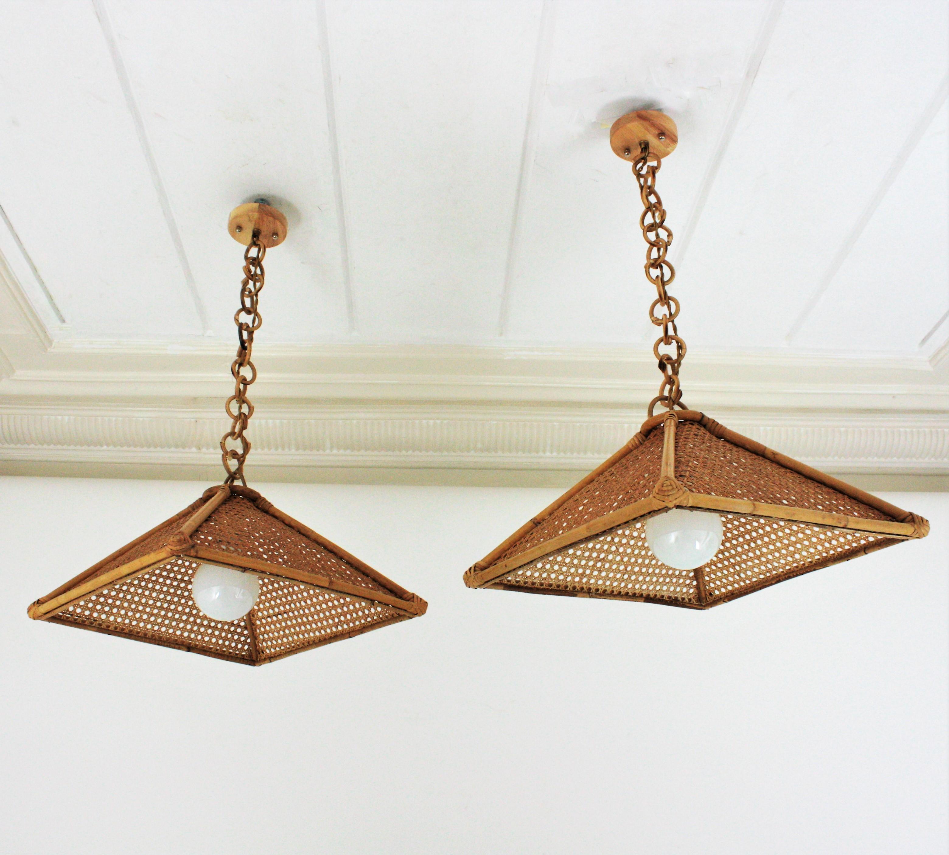 Pair of Mid-Century Modern woven wicker wire and rattan trapezoid shaped pendants / chandeliers. Spain, 1960s
This pair of suspension lamps feature a trapezoid rattan structure with wicker wire panels hanging from a chain with round rattan links
