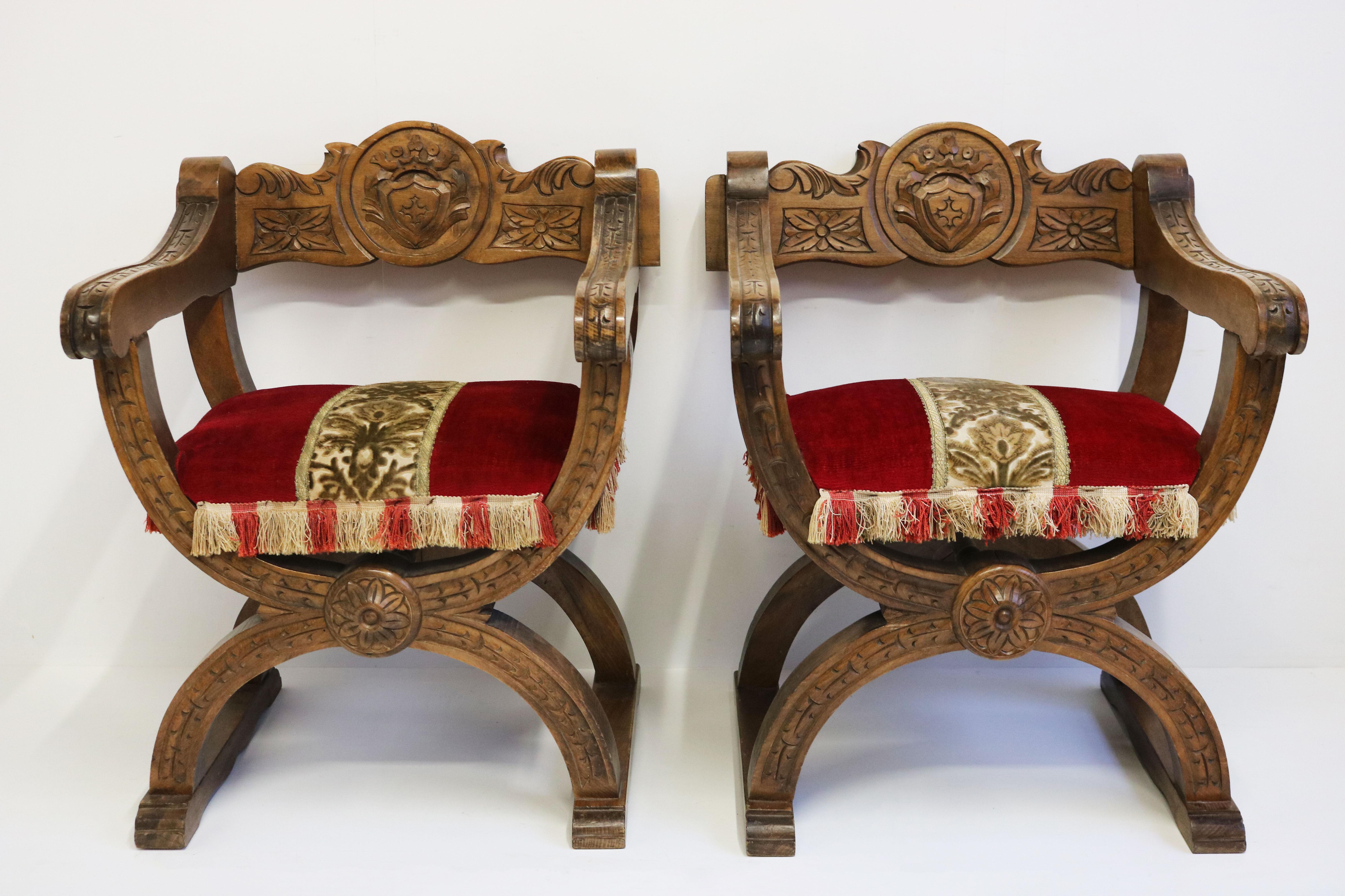Impressive pair of X frame throne / castle chairs in Spanish Medieval design style made in the 1930s. 
Solid oak frames with marvelous carved details , for example the knights emblem on the backrest.
Marvelous upholstery in red velvet with gold &