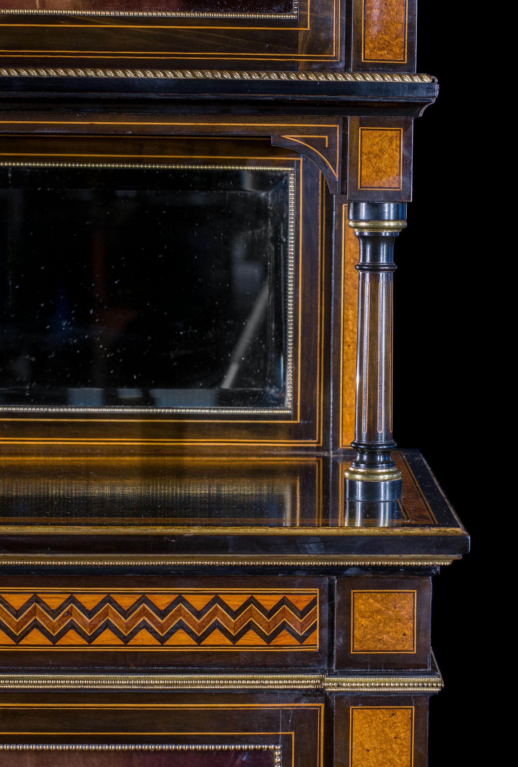 A pair of late Victorian display cabinets, ebonised and chequer inlaid with amboyna and purplewood, in the Aesthetic Movement style. Each cabinet has running gilt brass mounts, a baluster gallery above a pair of glazed doors enclosing two adjustable