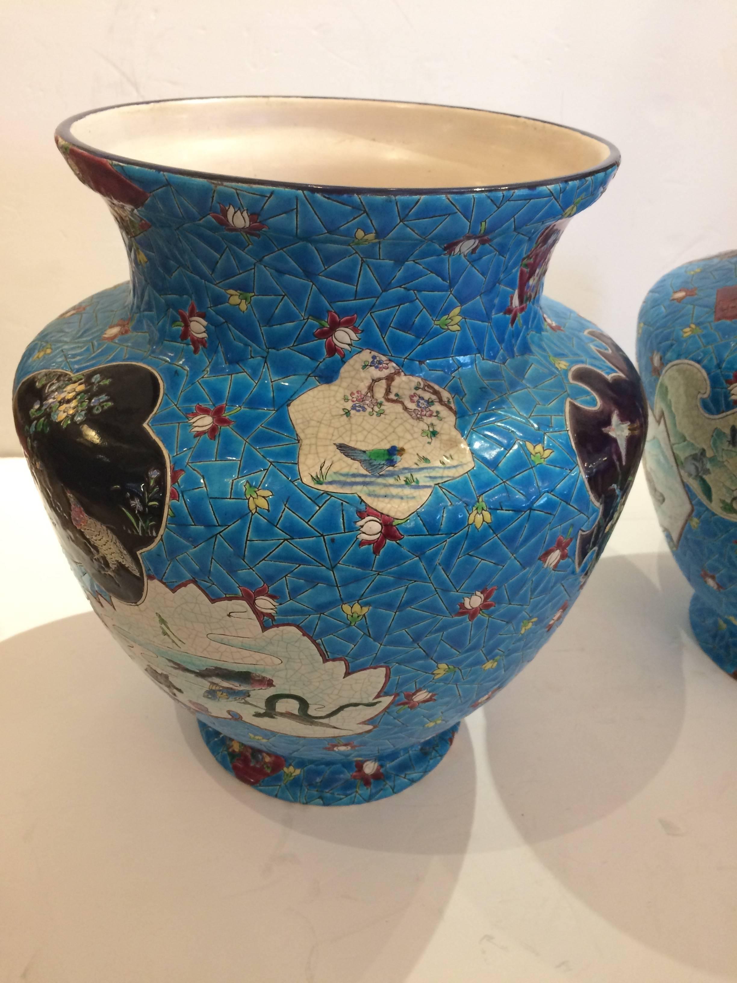 An impressive pair of very large French Longwy vases with meticulous detail having flowers, a figural scene, birds and a rooster in a glistening color palette of bright cerulean blue, black, white and maroon. One is stamped on the bottom. Opening is