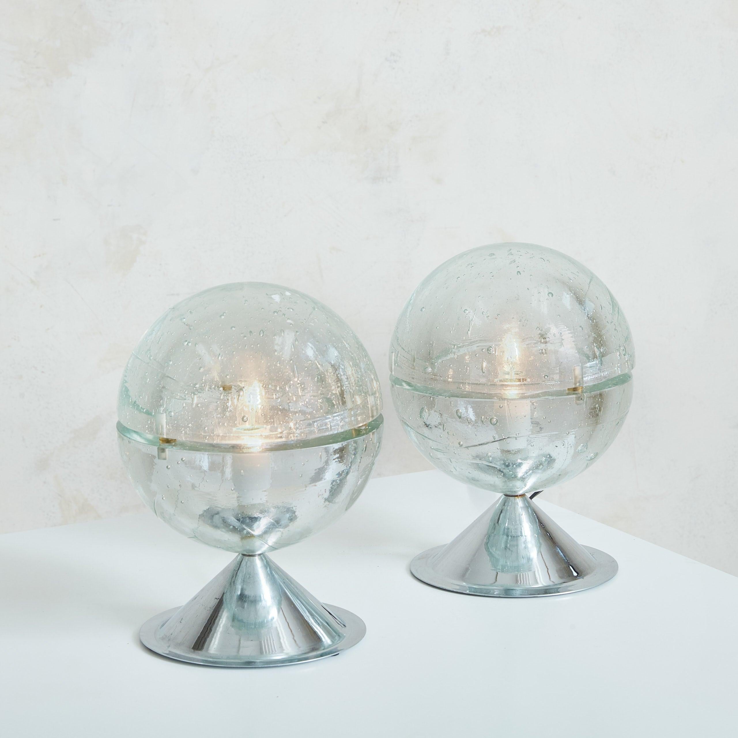 A striking pair of Italian spherical table lamps attributed to Albano Poli for Poliarte in 1968. These lamps are composed of two clear Murano glass hemispheres, each embedded with bubbles, creating a mesmerizing visual effect when illuminated. The