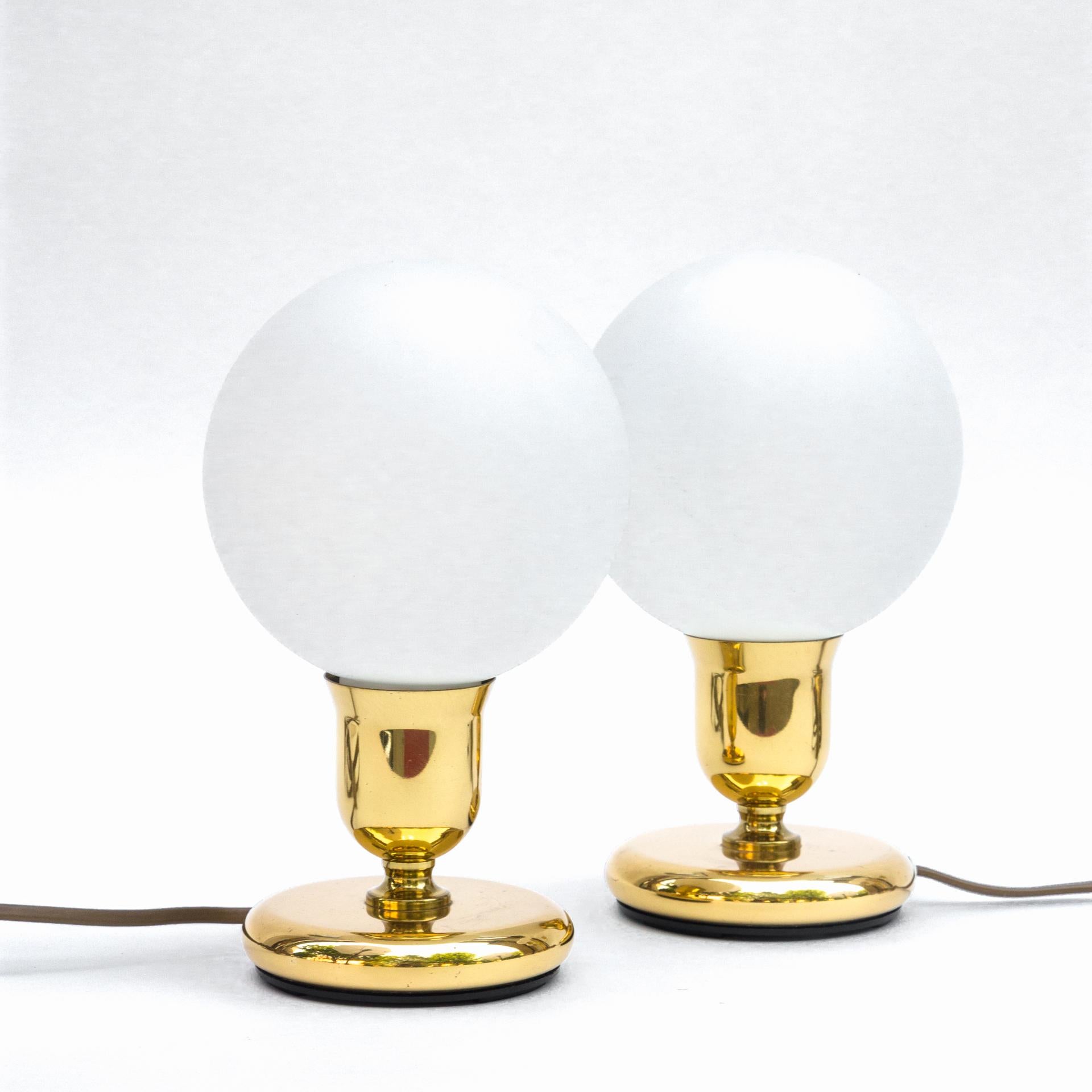 A set of two small lamps with spherical lampshades in the Art Deco type, from the 1970s. The bodies have a cup-like shape and on them are balls made of milky glass. The bodies have been reduced to flat, round bases from which the lampshade holder