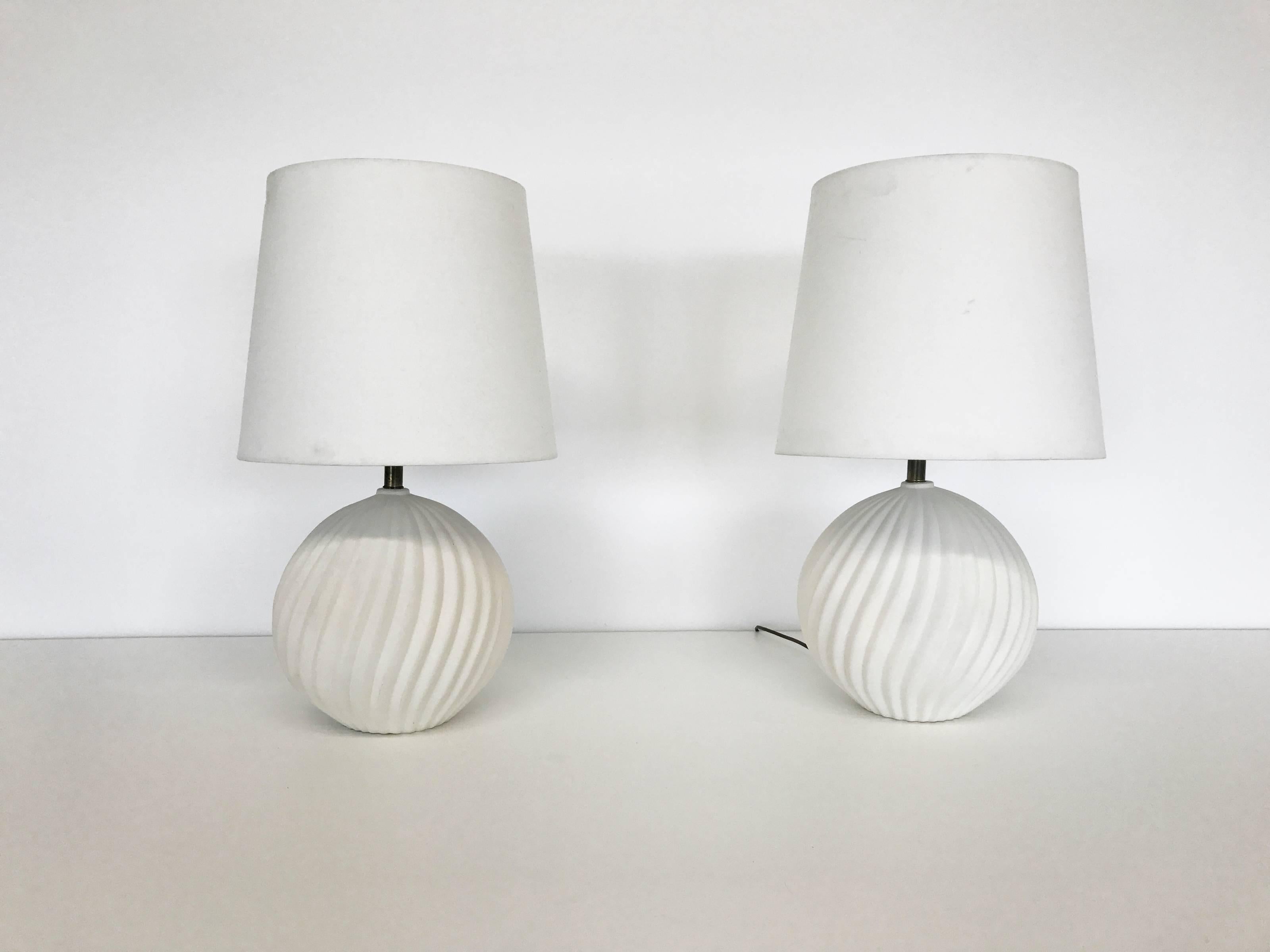 Pair of spherical ceramic lamps with twisted fluting. Lamp bodies are comprised of cream-colored unglazed ceramic with a matte finish. Brass neck and fittings. 

Lamps measure 16 in. high to top of bulb fitting and 12 in. diameter. Harps and