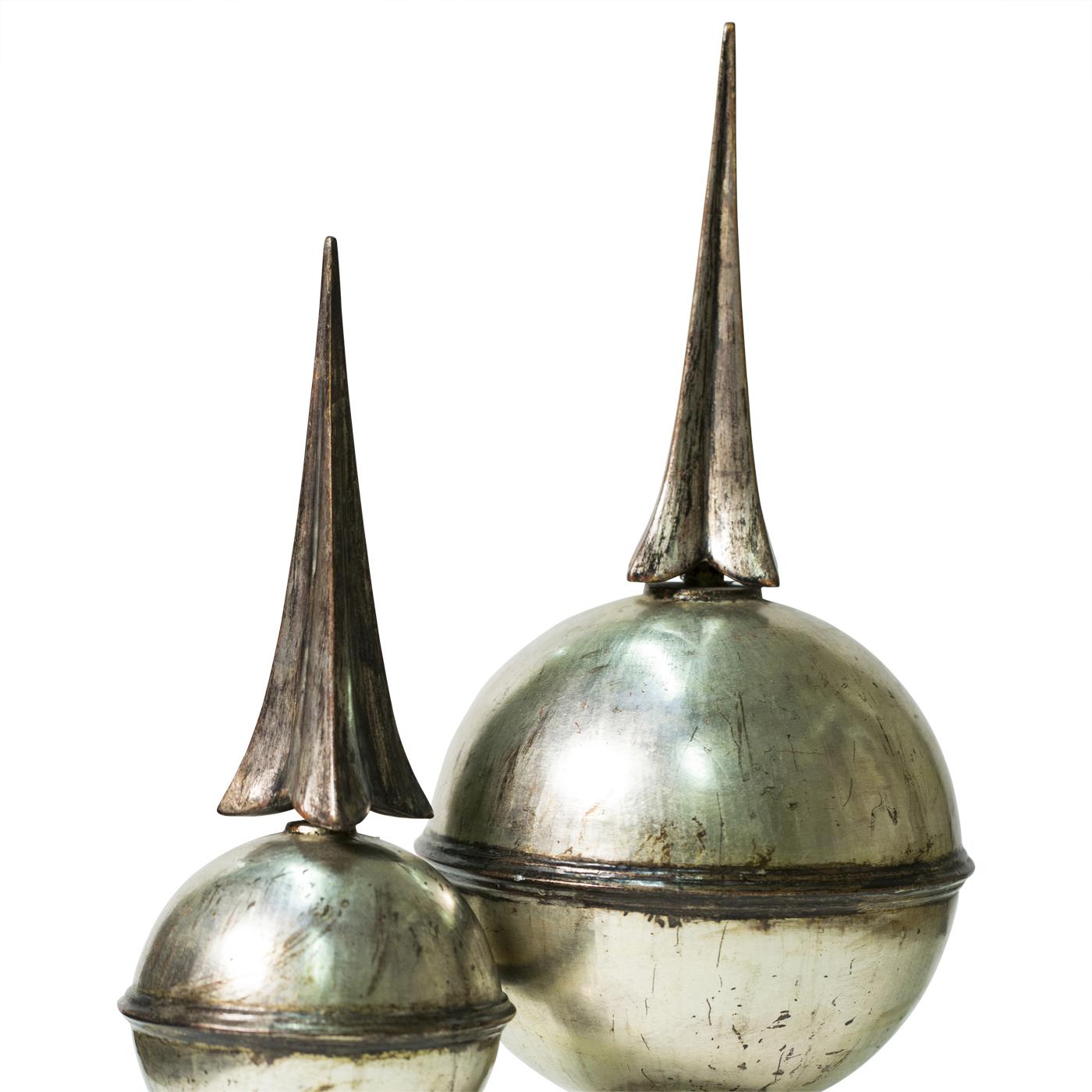 This pair of spherical ornaments adorned with spikes are an original design of master woodcarvers Castorina, inspired by similar objects found atop chimneys and bell-towers. The pieces are entirely carved by hand and finished in silver leaf for a