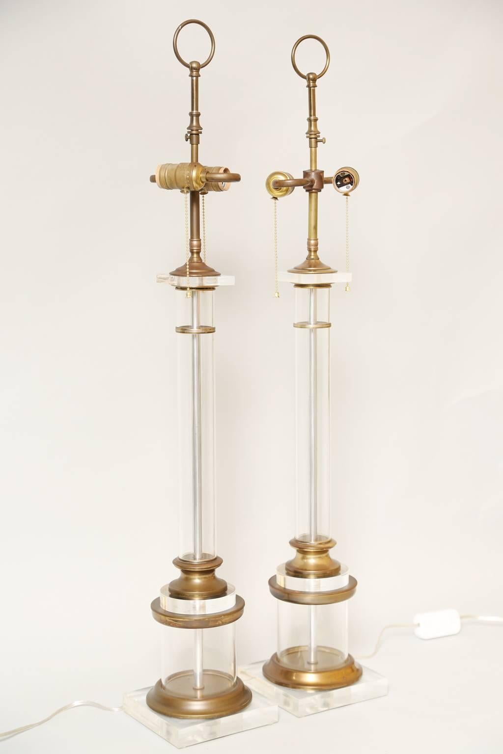 Pair of table lamps, each a round column of clear acrylic Lucite, with collars and fittings of brass, raised on square plinth base. 

Stock ID: D1256.