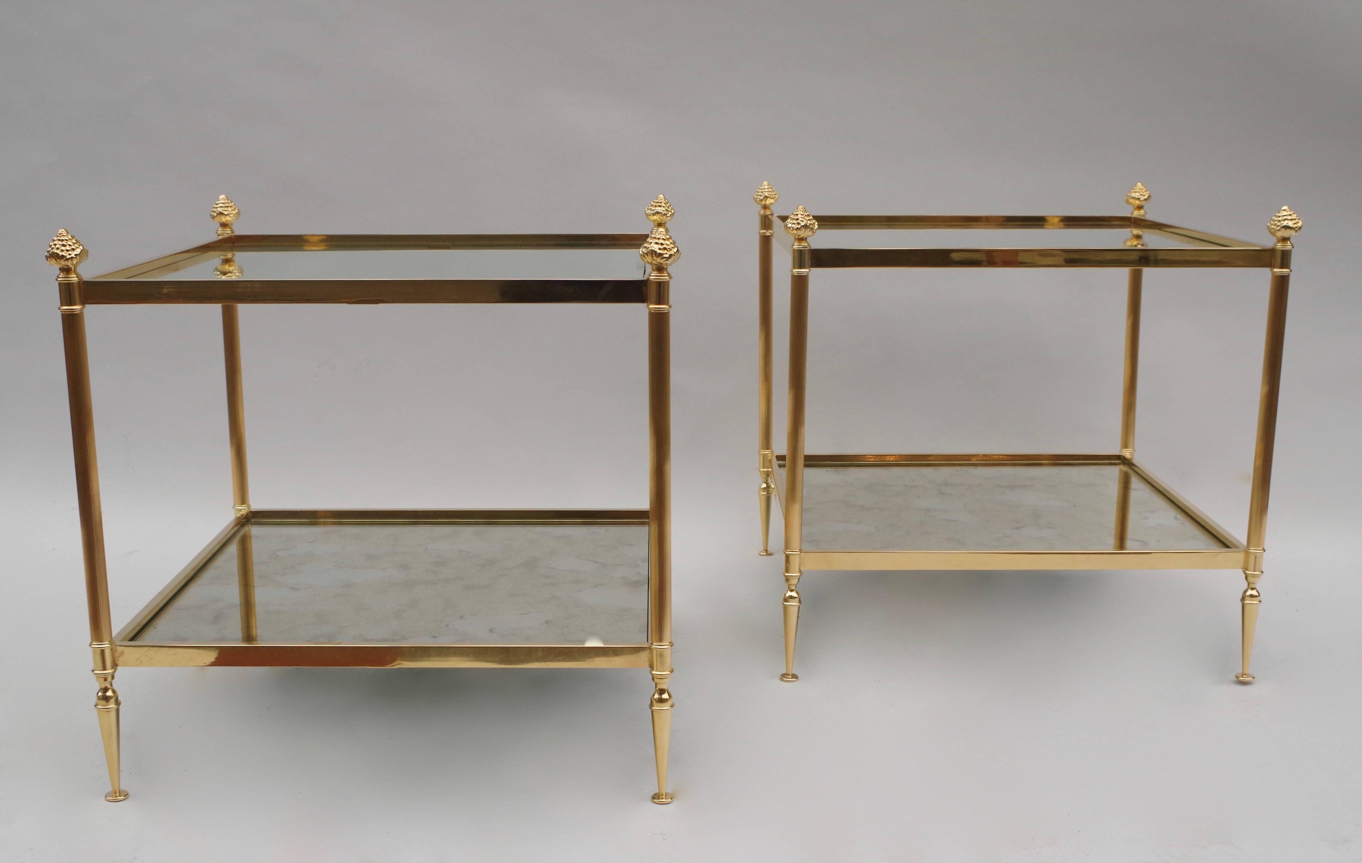 Pair of square gilt brass side tables realized, circa 1970, in the taste of the Maison Jansen.
Standing on four baluster legs, inferior tray in oxidized mirror and joined with straight uprights to the glass top, framed with four pine-cone capping