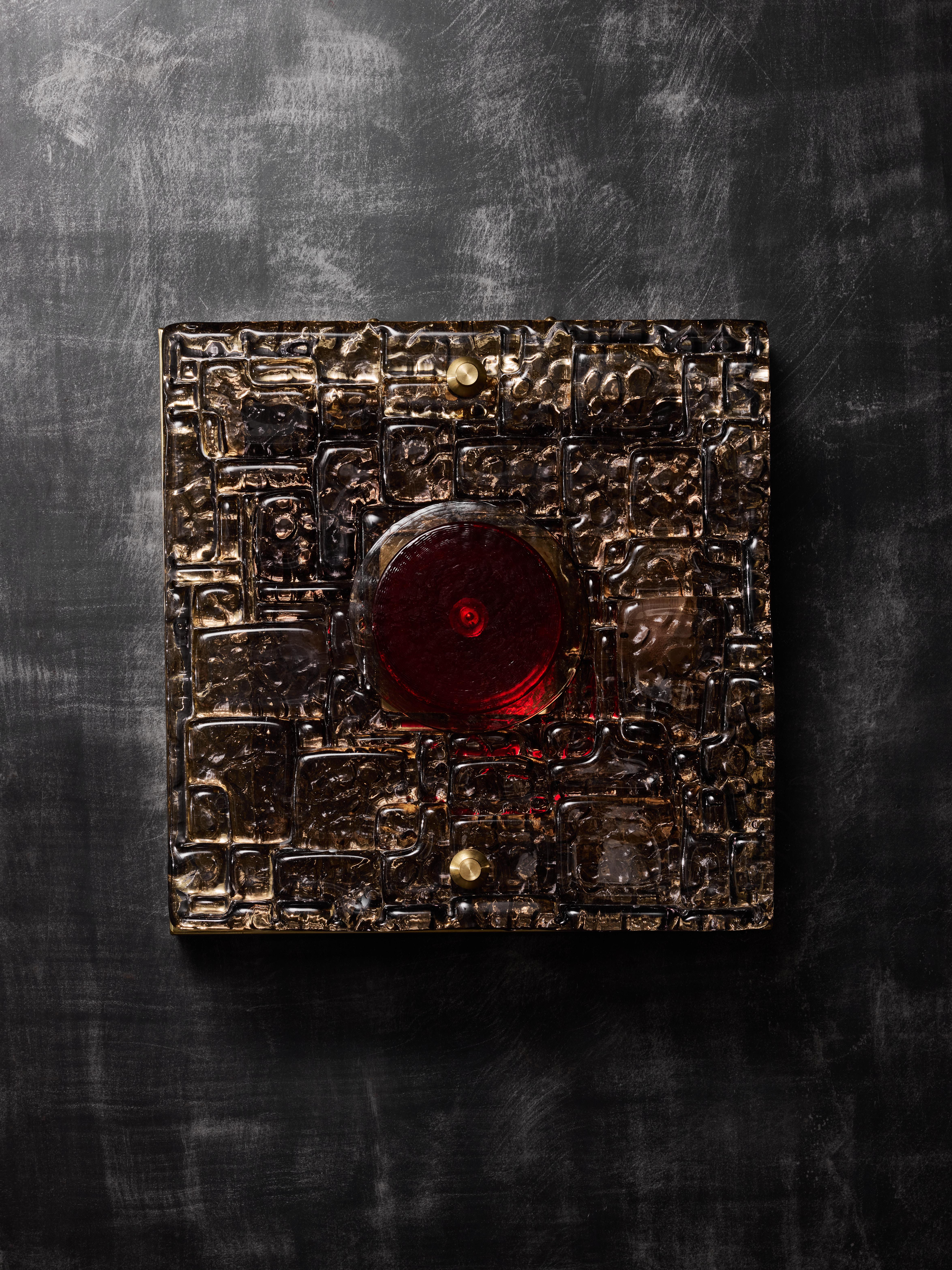 Pair of wall sconces made of a square brass structure, two sources of light hidden behind a slab of patterned Murano glass and a central red glass disc in the middle.
