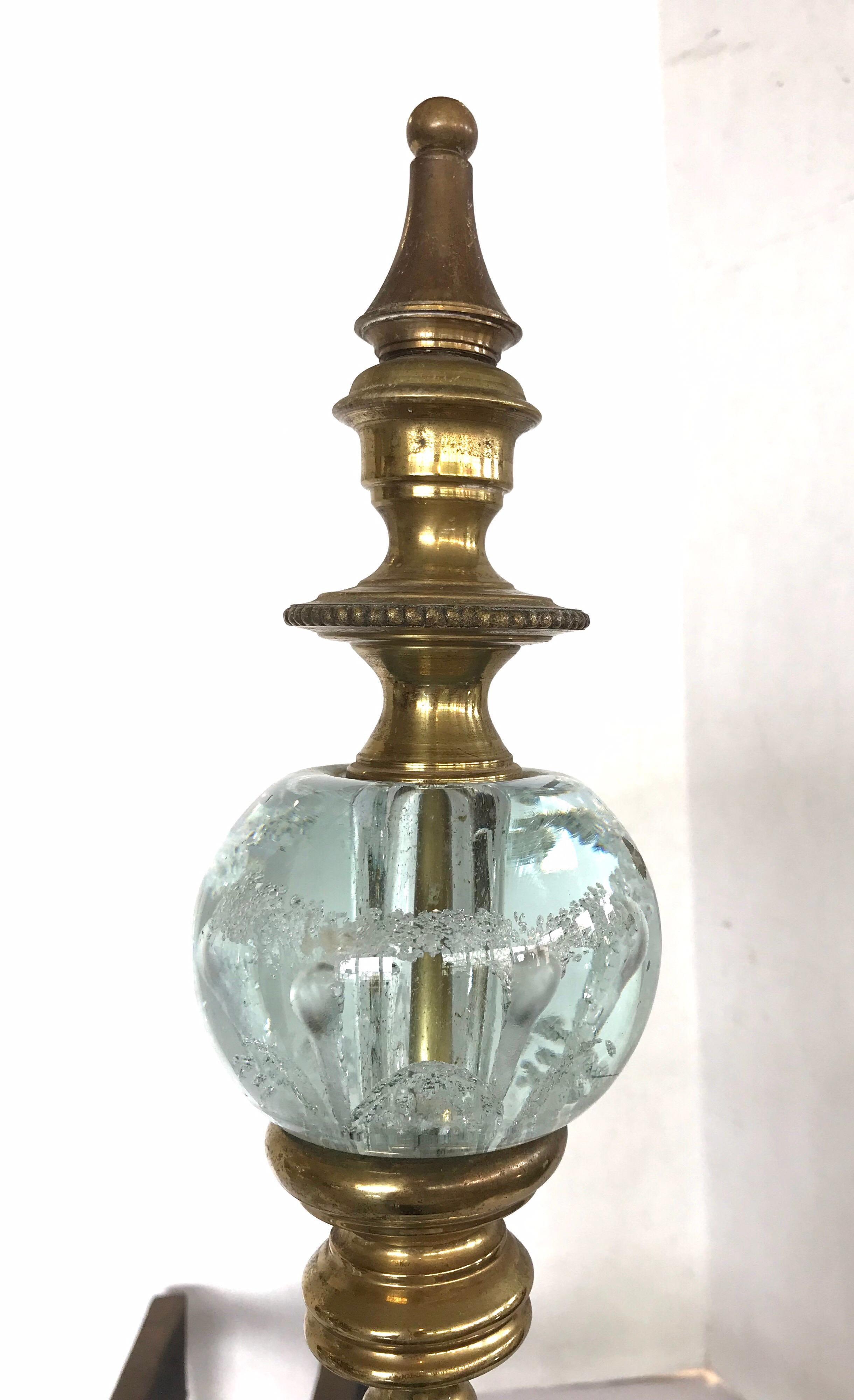 Beautiful St. Clair andirons feature brass finial tops and pedestals with crystal paperweight accents on scrolling brass feet with cast iron log stops. The color of the crystal is a very light blue, almost the color of water.