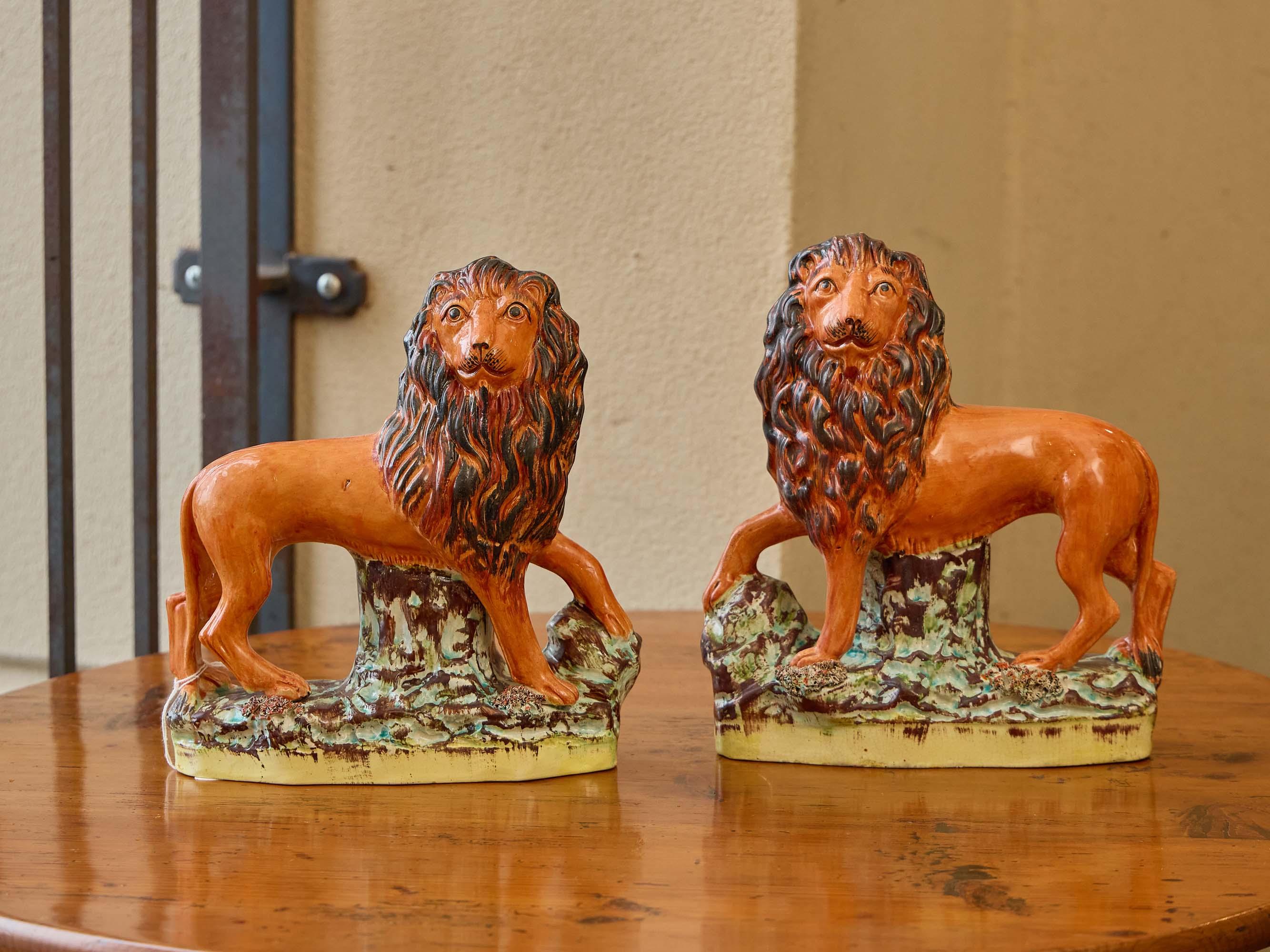 Ein lebhaftes und wunderbar ausdrucksstarkes Paar Staffordshire-Töpferlöwen aus der Zeit um 1870, die spiegelbildlich modelliert sind und stolz auf naturalistischen Sockeln stehen. Ihre hellen ockerfarbenen Körper kontrastieren kühn mit den tief