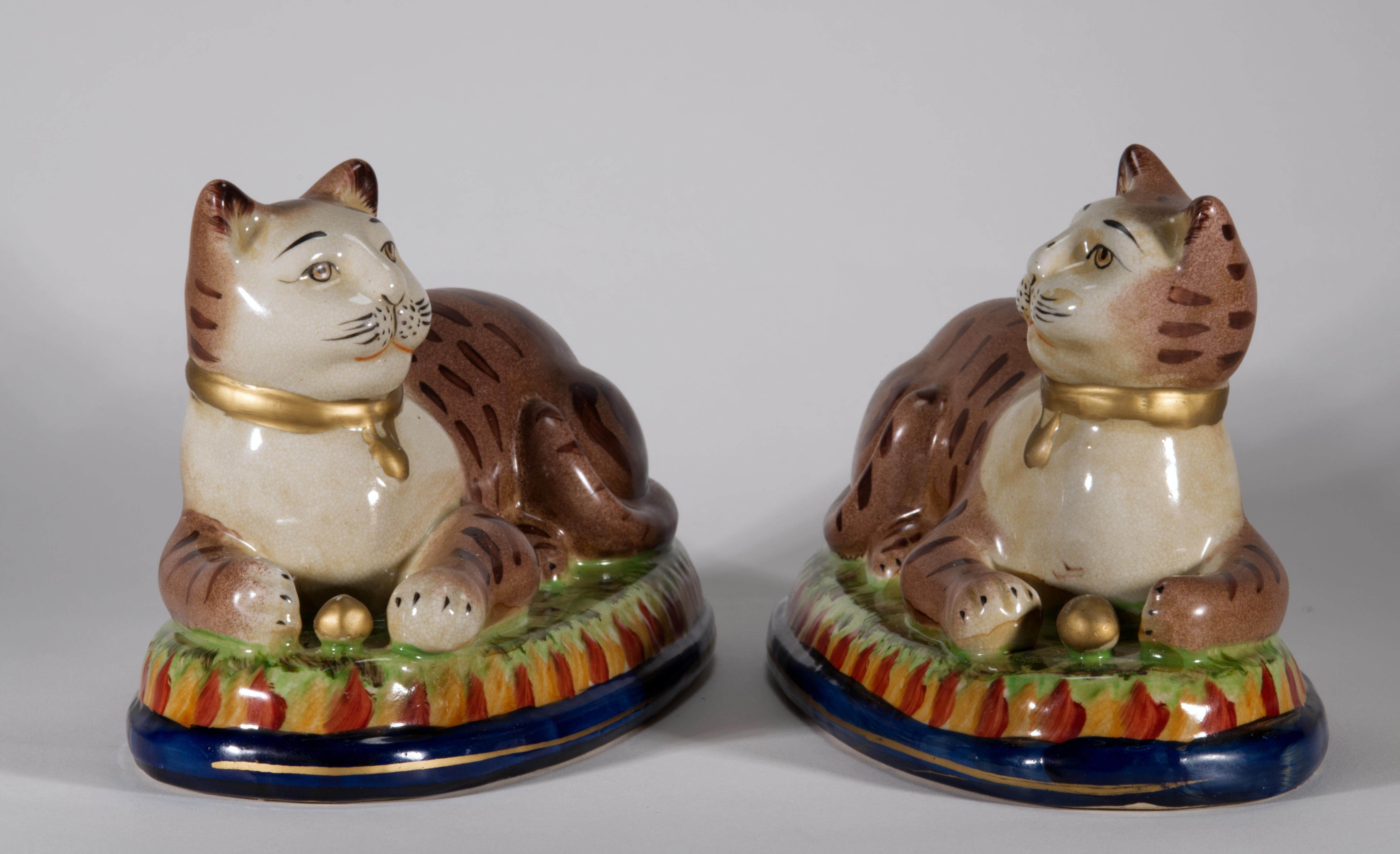  Vintage By Staffordshire Katzenskulpturen zeigen die rechte und die linke gestromte Katze (so wie sie ausgestellt werden), die auf ovalen Kissen ruhen und mit ihren Vorderpfoten kleine goldene Kugeln halten. Die Katzen tragen goldene Halsbänder mit