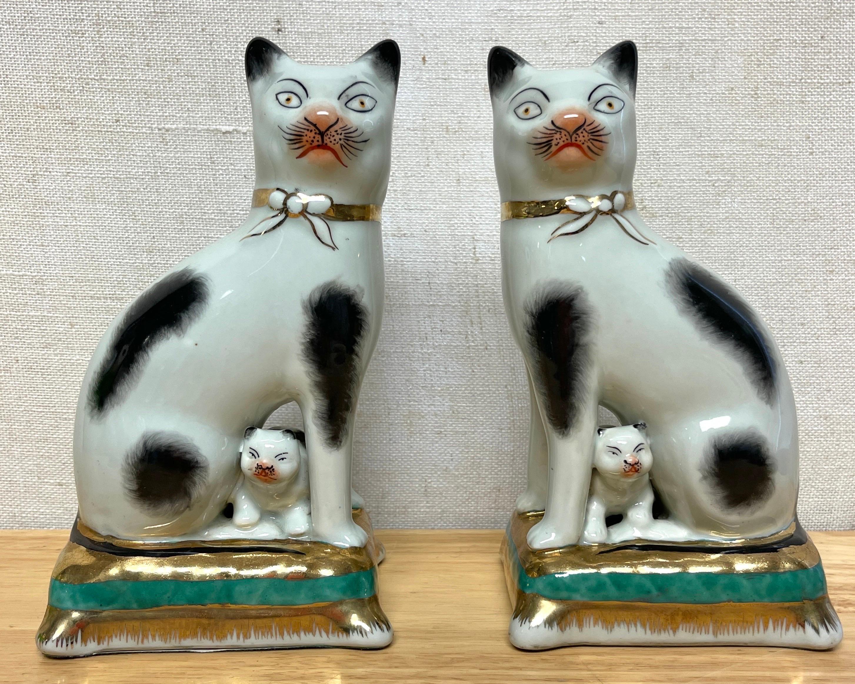 Pair of Staffordshire Figures of Seated Black & White Cats with Kittens 
England, 20th Century 

Rare examples, Each one a well painted feline with expressive faces, with kittens in between their legs, seated on gilt green tasseled cushions.