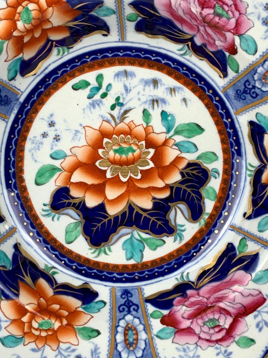 Made circa 1825, this pair of eye-catching dishes features a lovely orange lotus blossom at the center and six pink and orange lotus blossoms decorating the border.
Each blossom sits above cobalt blue leaves, lined with gilt. Small green leaves add