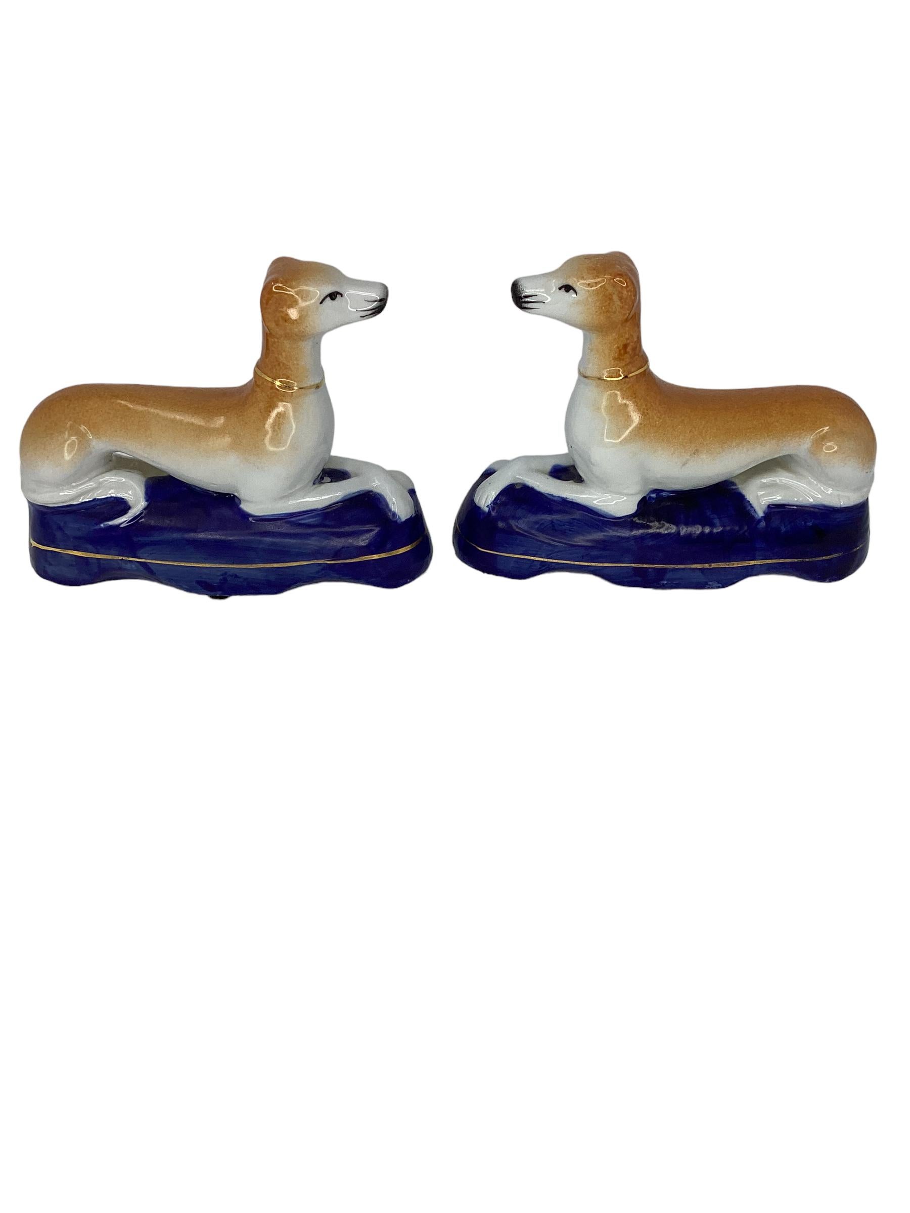 A wonderful Pair of Staffordshire Pottery Greyhound or Whippets in a recumbent pose with crossed legs. Dogs are shown laying on a blue base.