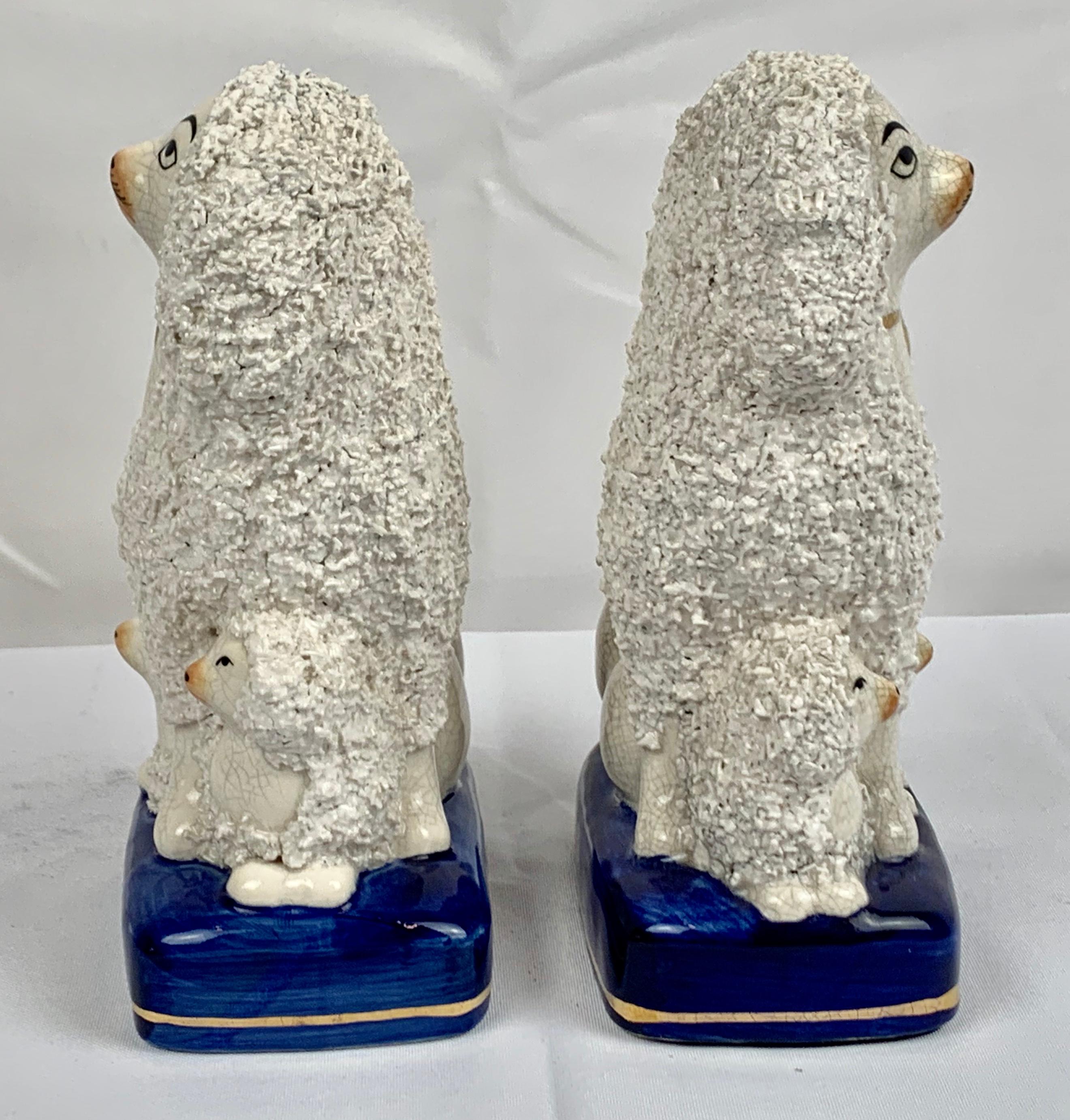 Pair of white Staffordshire poodles with their four pups sitting on cobalt blue bases trimmed with a gold line. Their bodies are covered with bocage, which was to represent fur. The male and female poodles are both wearing the tradirional collar