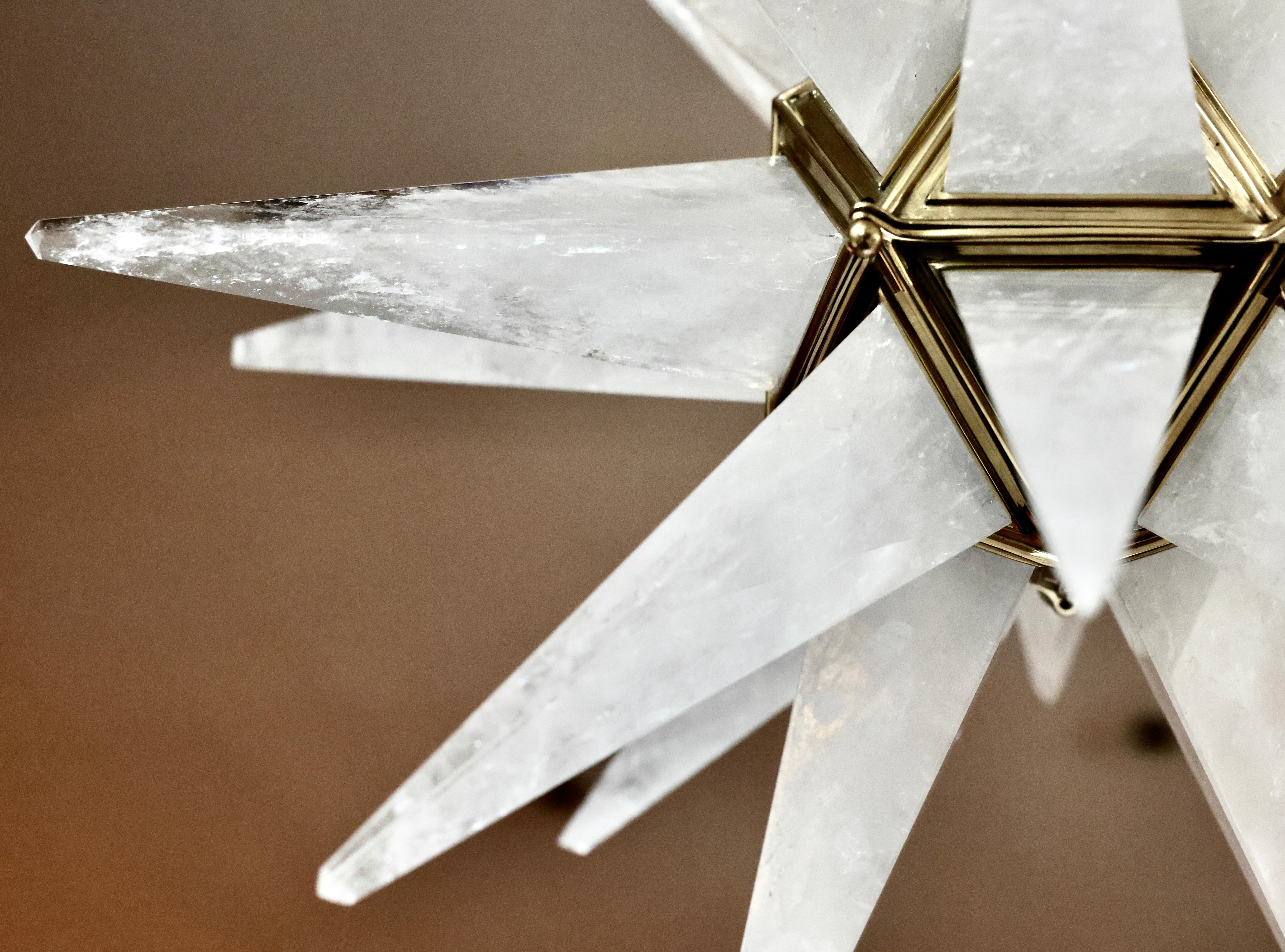 Pair of finely carved star form rock crystal chandeliers with polished brass finish frames. Created by Phoenix Gallery, NYC.
Height adjustable.

Each fixture has installed 2 candelabra sockets, 60 watts each, 120 watts total. 
Metal finish and