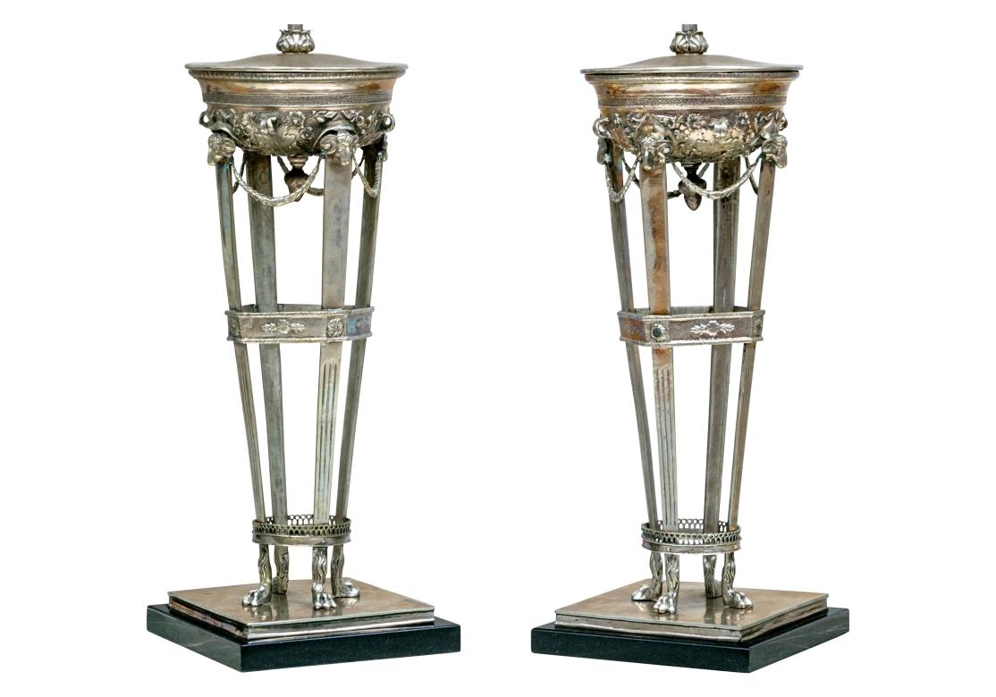 A very fine pair of Neoclassical style Lyle and Umbach Pompeiian and French Empire style table lamps showcasing white bronze Athenian forms with lidded urn-shaped fonts heavily decorated with foliate relief around the bottoms leading to spade