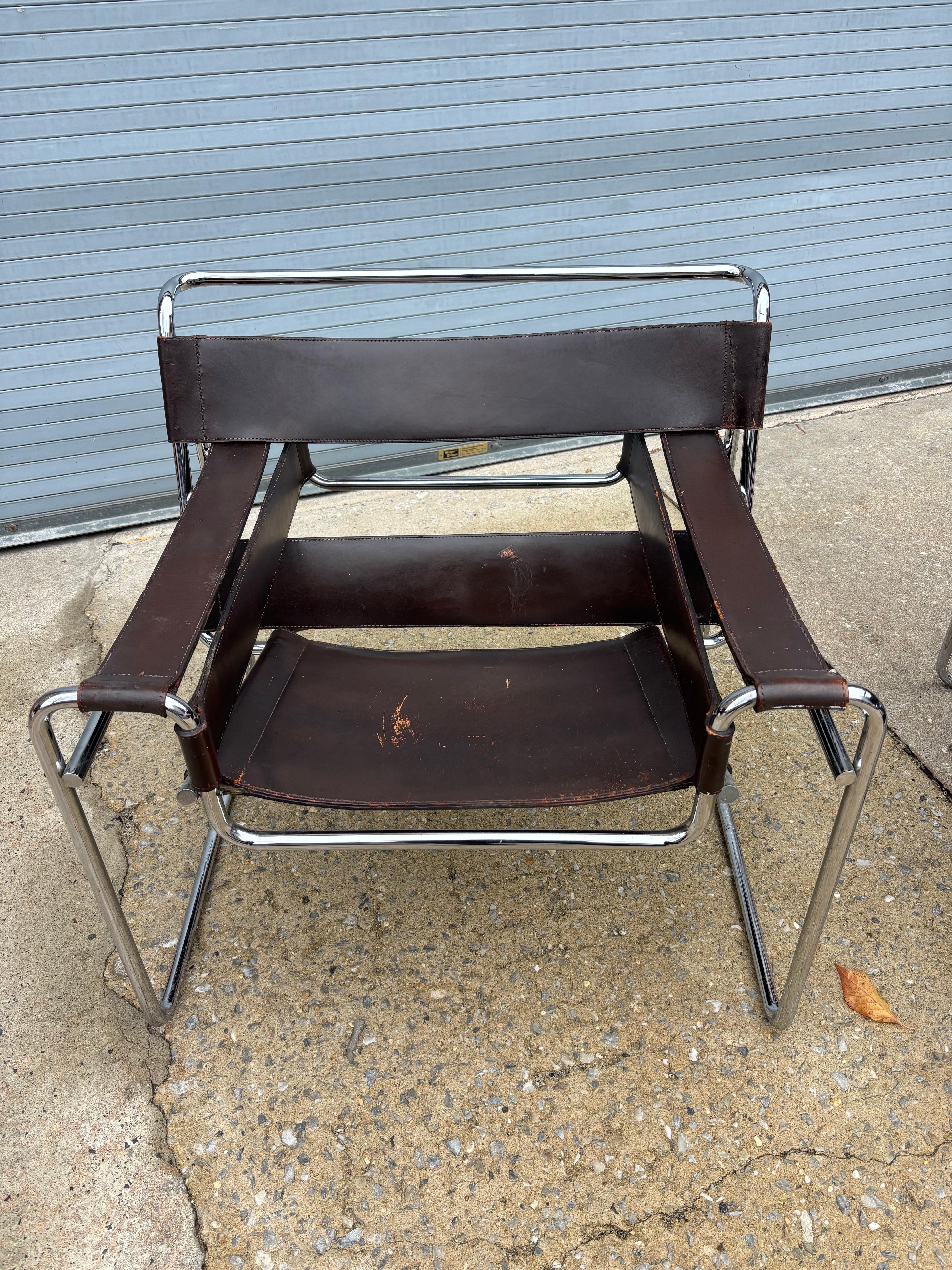 Bonita pareja de primeras sillas Waselie vendidas de pie. Las sillas datan de principios de los años 60 en un cuero marrón chocolate que muestra mucha personalidad y pátina. Se han realizado algunos pespuntes nuevos en las costuras, probablemente