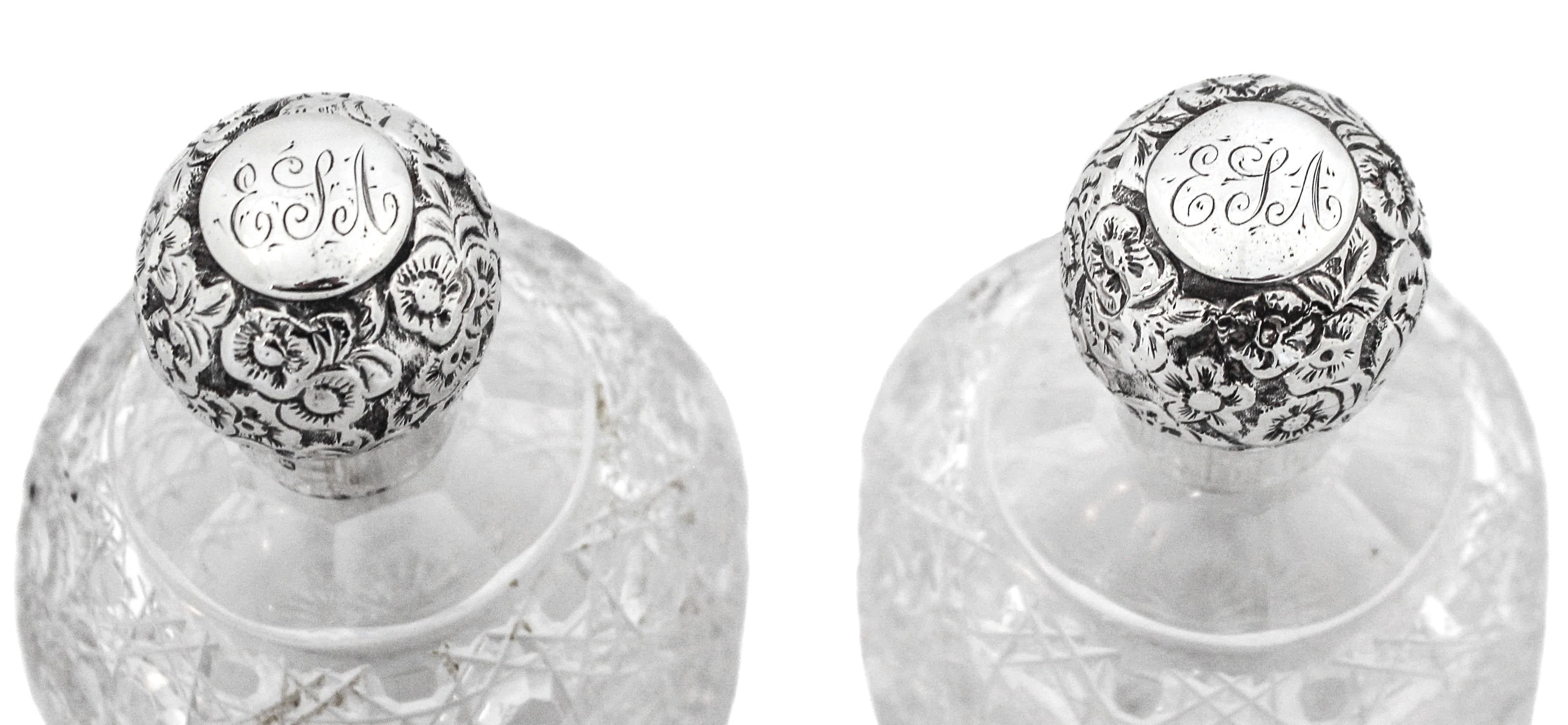 A pair of sterling silver and crystal perfume bottles made in England, circa 1907. Each bottle has an elaborate cut-glass design with sterling silver tops. The sterling top unscrews and has a floral Repousse pattern. These beautiful pieces would
