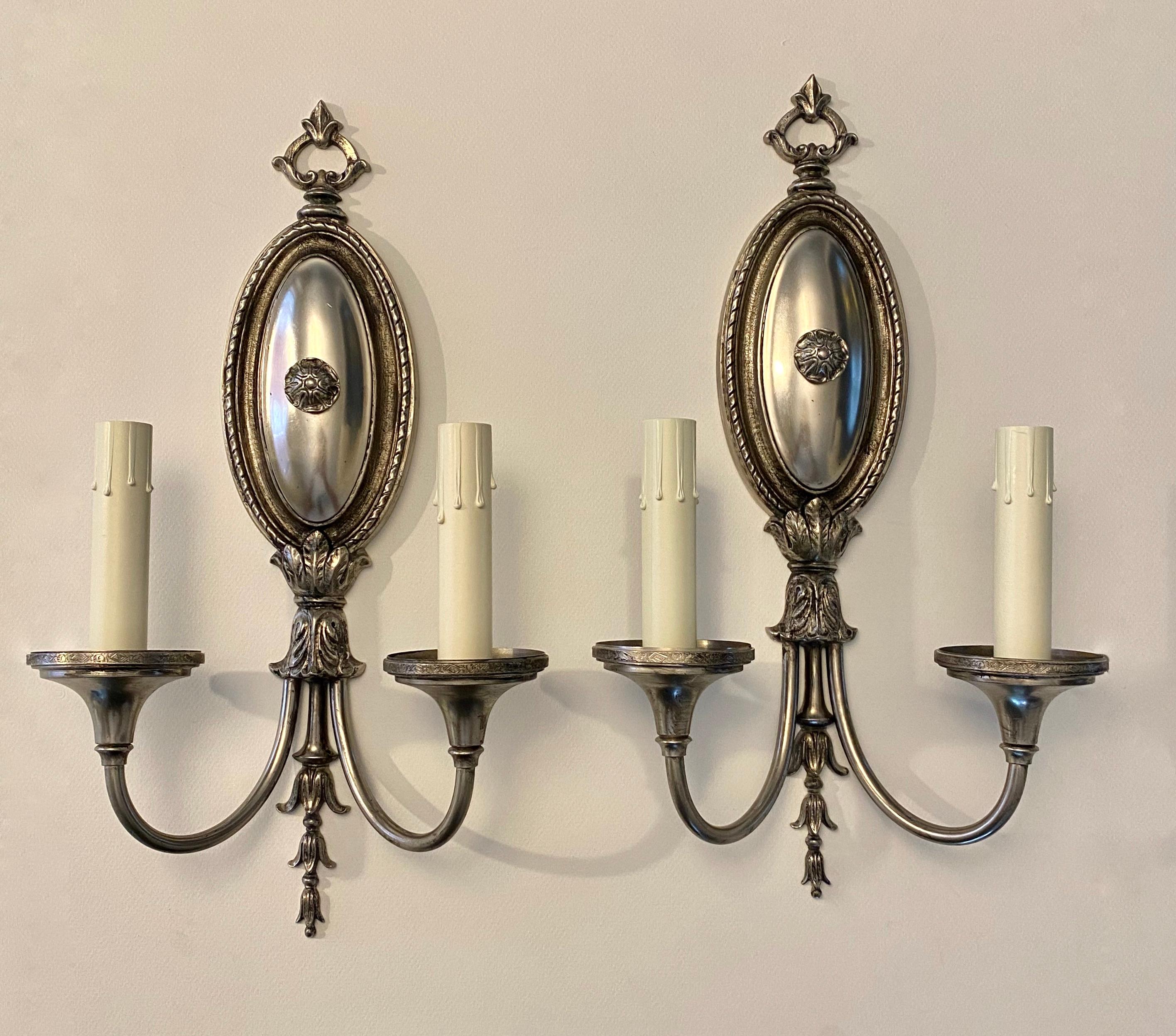 Pair of Adam style two-arm wall sconces attributed to Sterling Bronze Company, New York in an antiqued nickel finish. Beautiful scrolled acanthus leaves at arms and candle cups have a delicate incised pattern to edges. Each sconce uses two