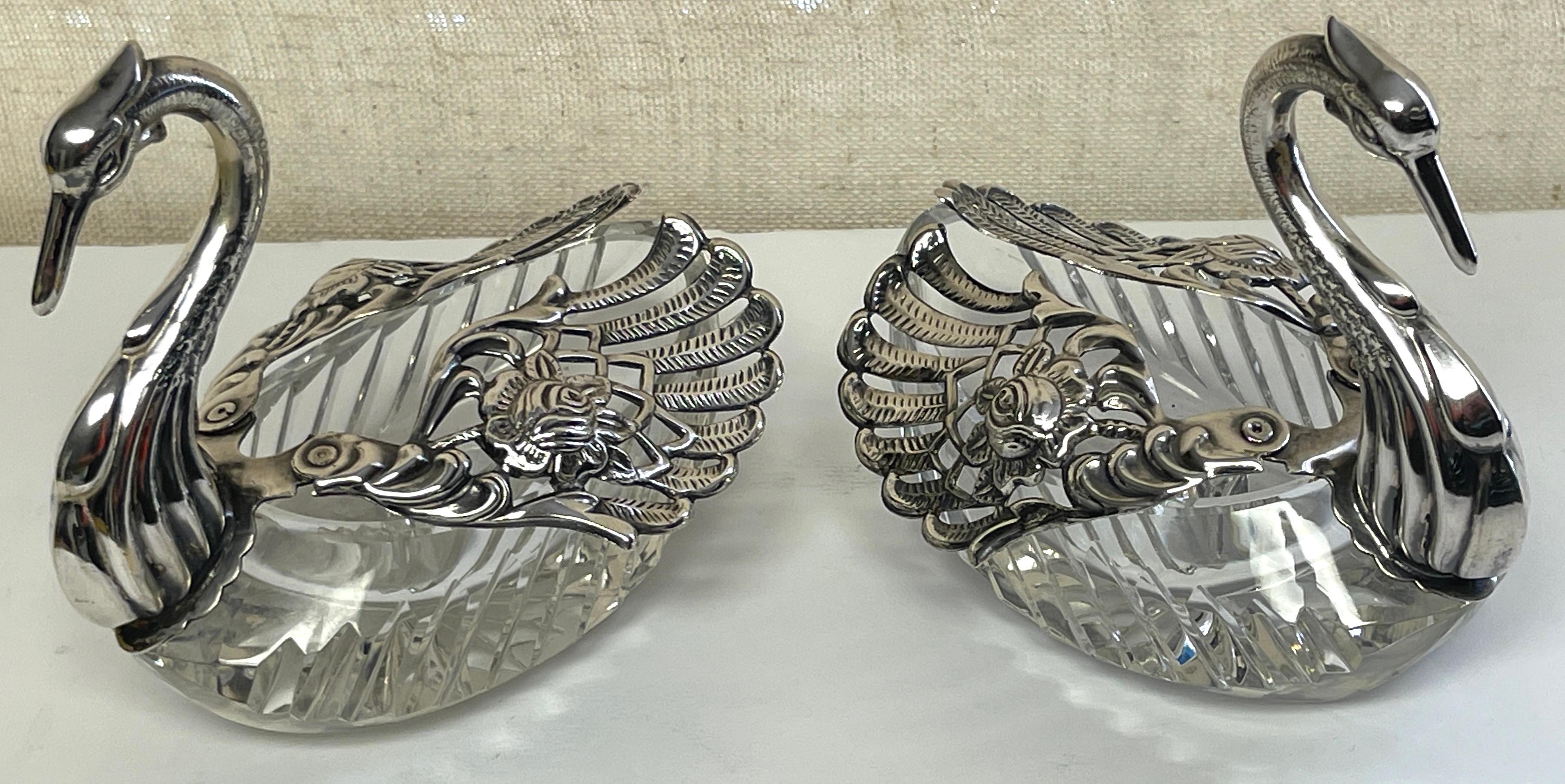 Pair of sterling & crystal swan sweetmeat dishes 
Each one of realistically cast and modeled, the graceful swans cast in sterling silver, with articulated pierced wings that expand 6-inches wide, resting and cut crystal bottoms 
Each swan measures