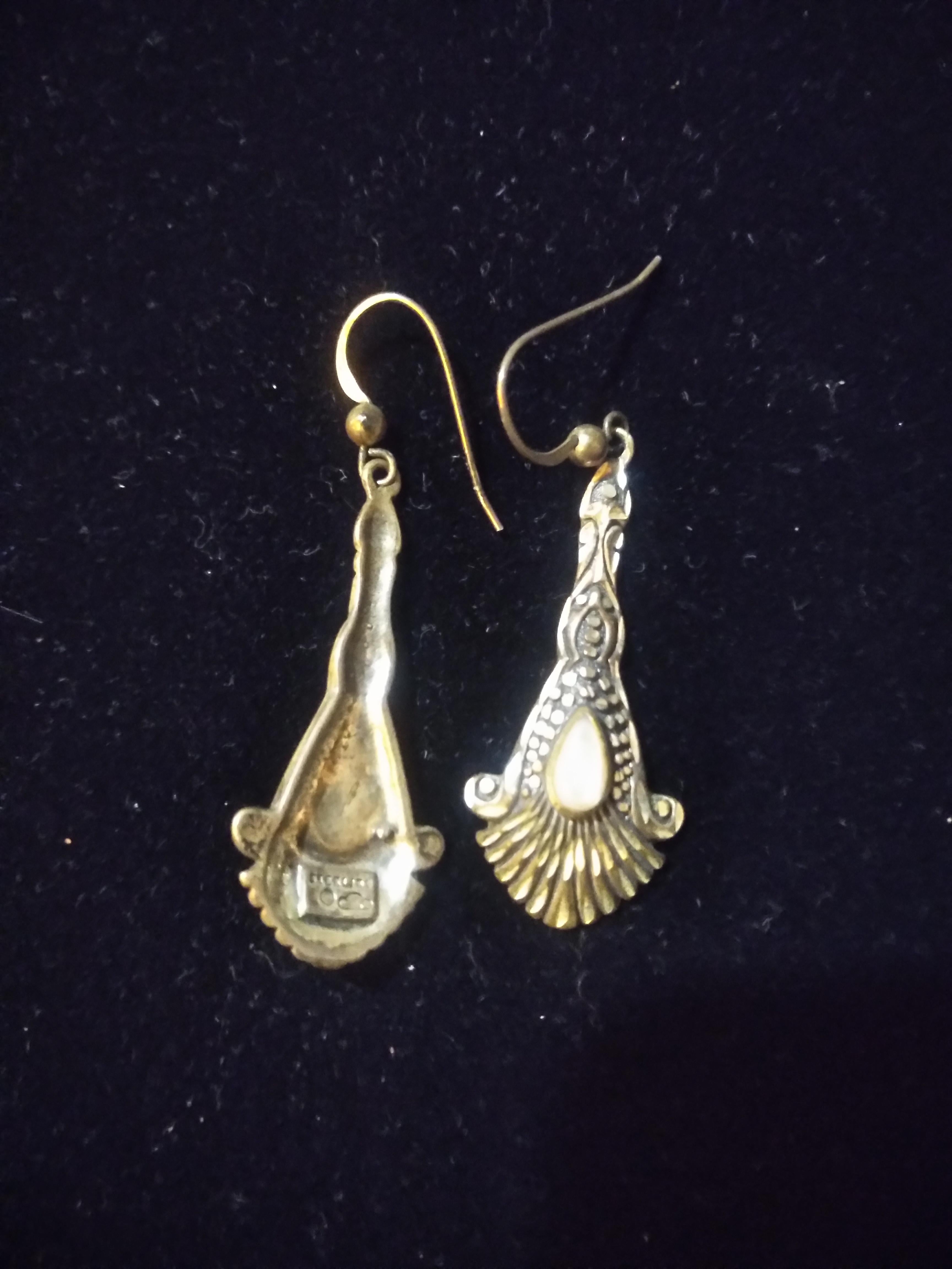 These earrings are made in an Art Nouveau Style. They're made of sterling silver and have marcasite accents. They have a white stone setting.