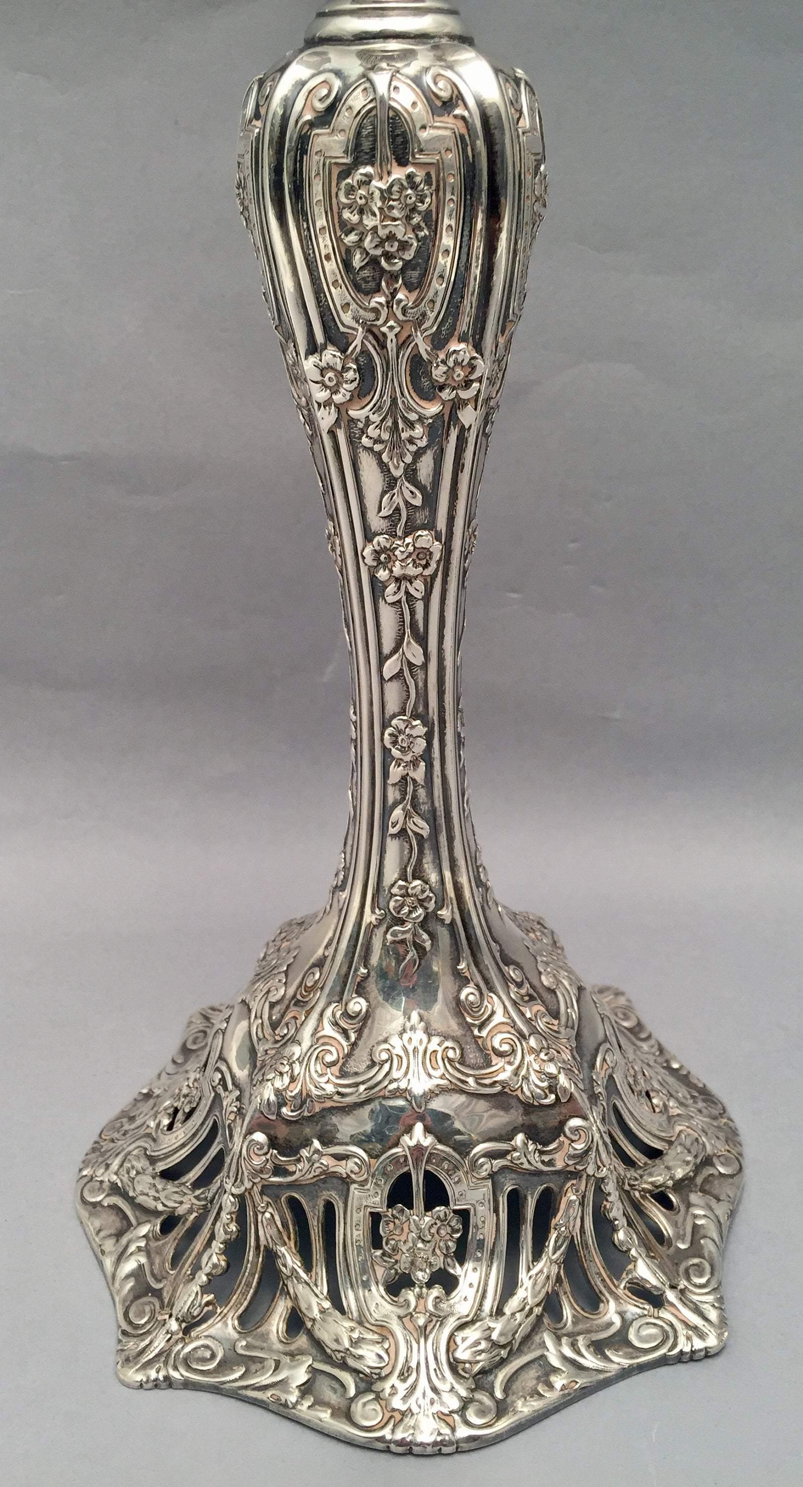 Pair of 20th century American weighted sterling silver candlesticks by Theodore B. Starr, ,having a baluster column with urn form capital, and profusely decorated with tooled and applied swags, flowers, foliage and shields on an openwork base.