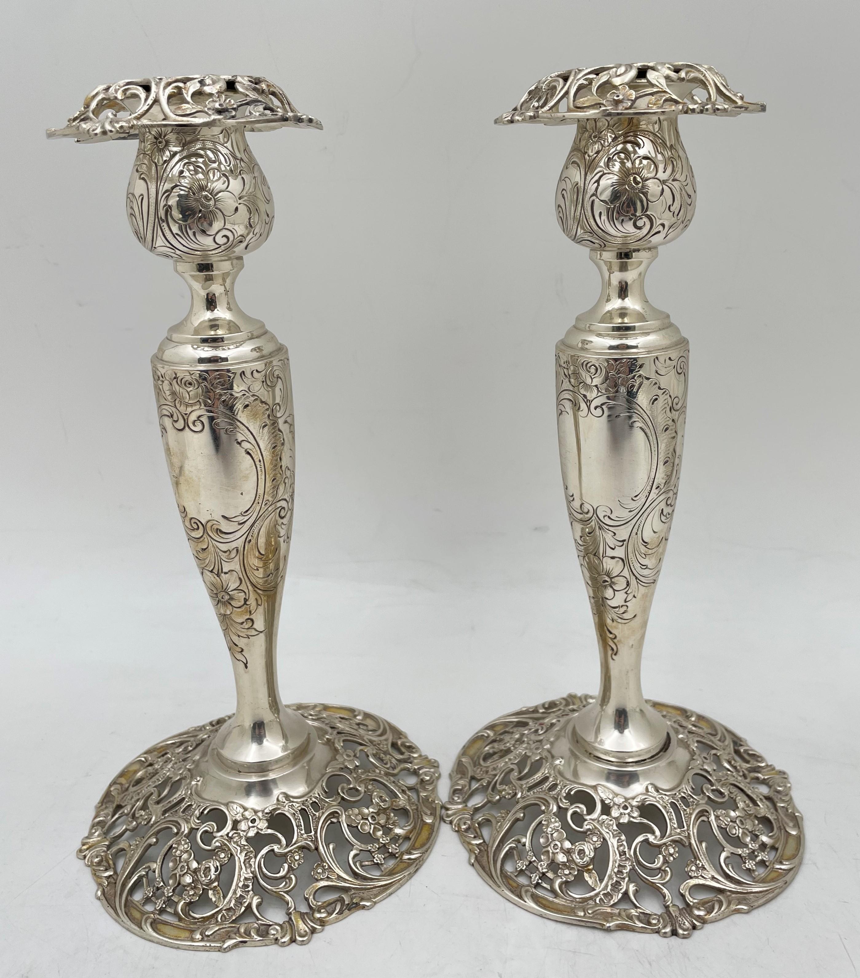 Pair of American, sterling silver candlesticks, presumably from the early 20th century, in Art Nouveau style with exquisite floral motifs adorning the body as well as the pierced rim and base. They Measure 9'' in height by 4 3/4'' in diameter at the