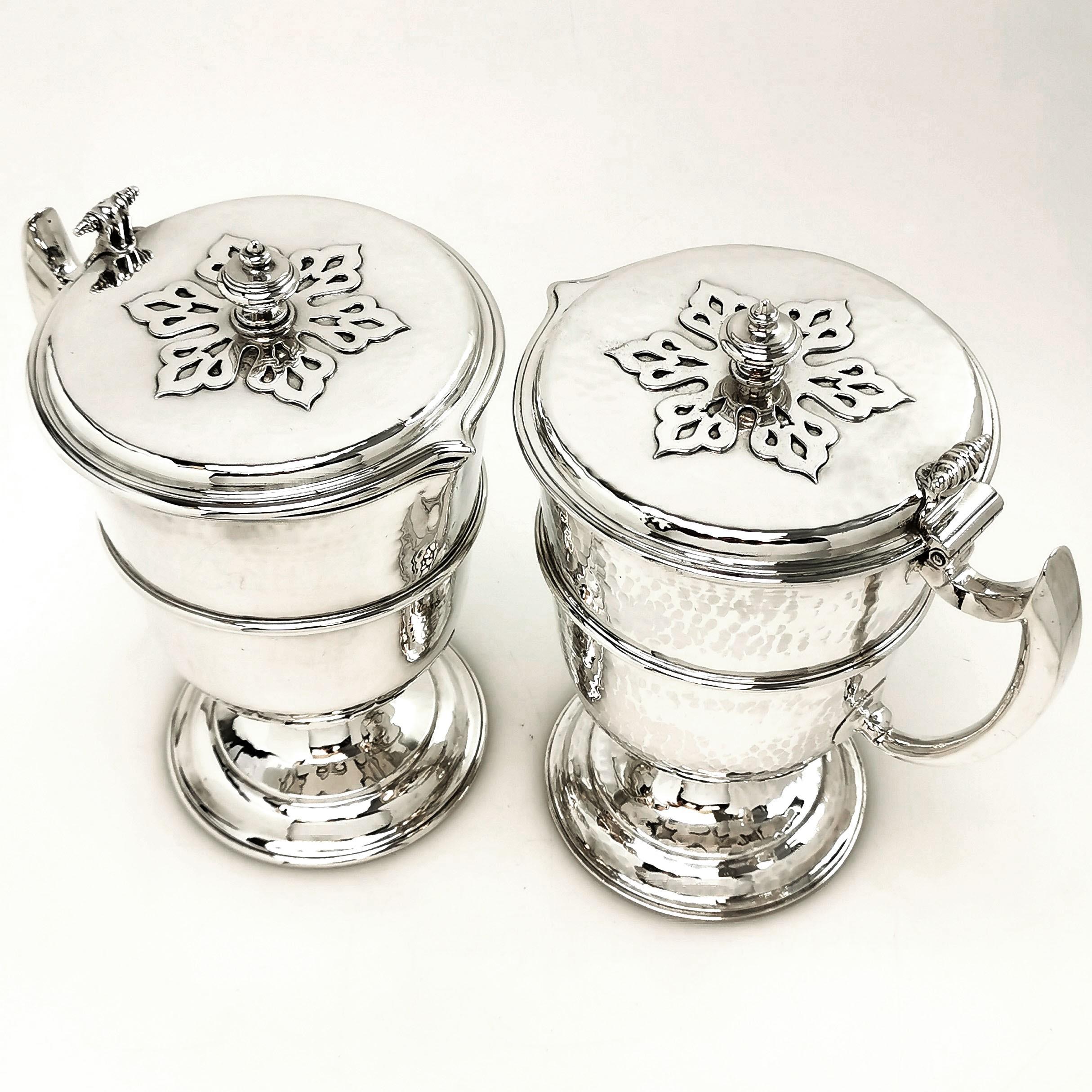 A gorgeous pair of Antique Solid Silver Jugs created in the style of William and Mary late 17th century style. Each Jug has a hinged lid with an applied pattern on the lid. The bodies feature a delicate hammered effect and each jug stands on spread