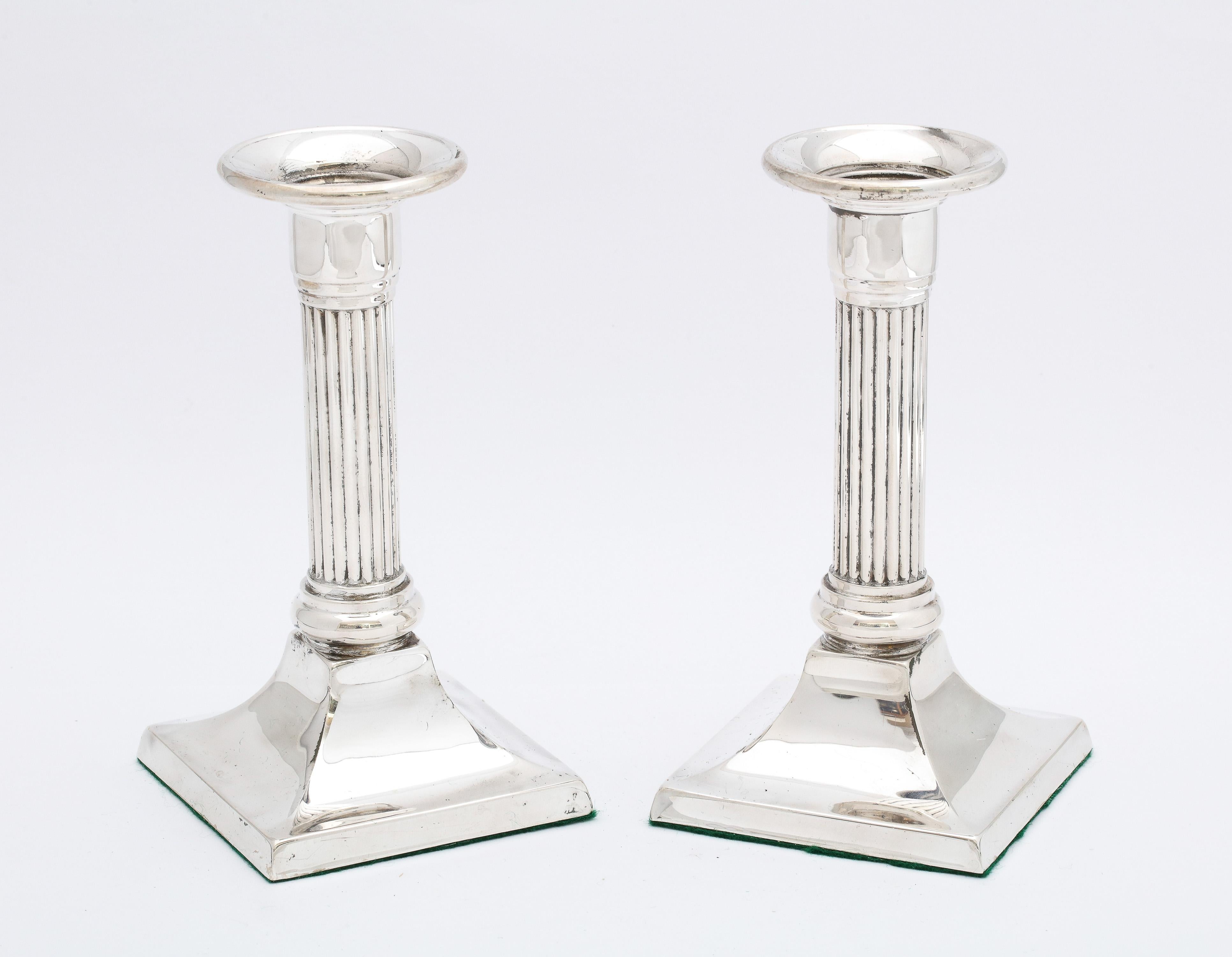 Pair of sterling silver, Neoclassical-Style, column-form candlesticks, American, Ca. 1930's. Each candlestick measures 5 3/4 inches high x 3  inches deep (at deepest point) x 3 inches wide (at widest point) . Weighted. The underside of each