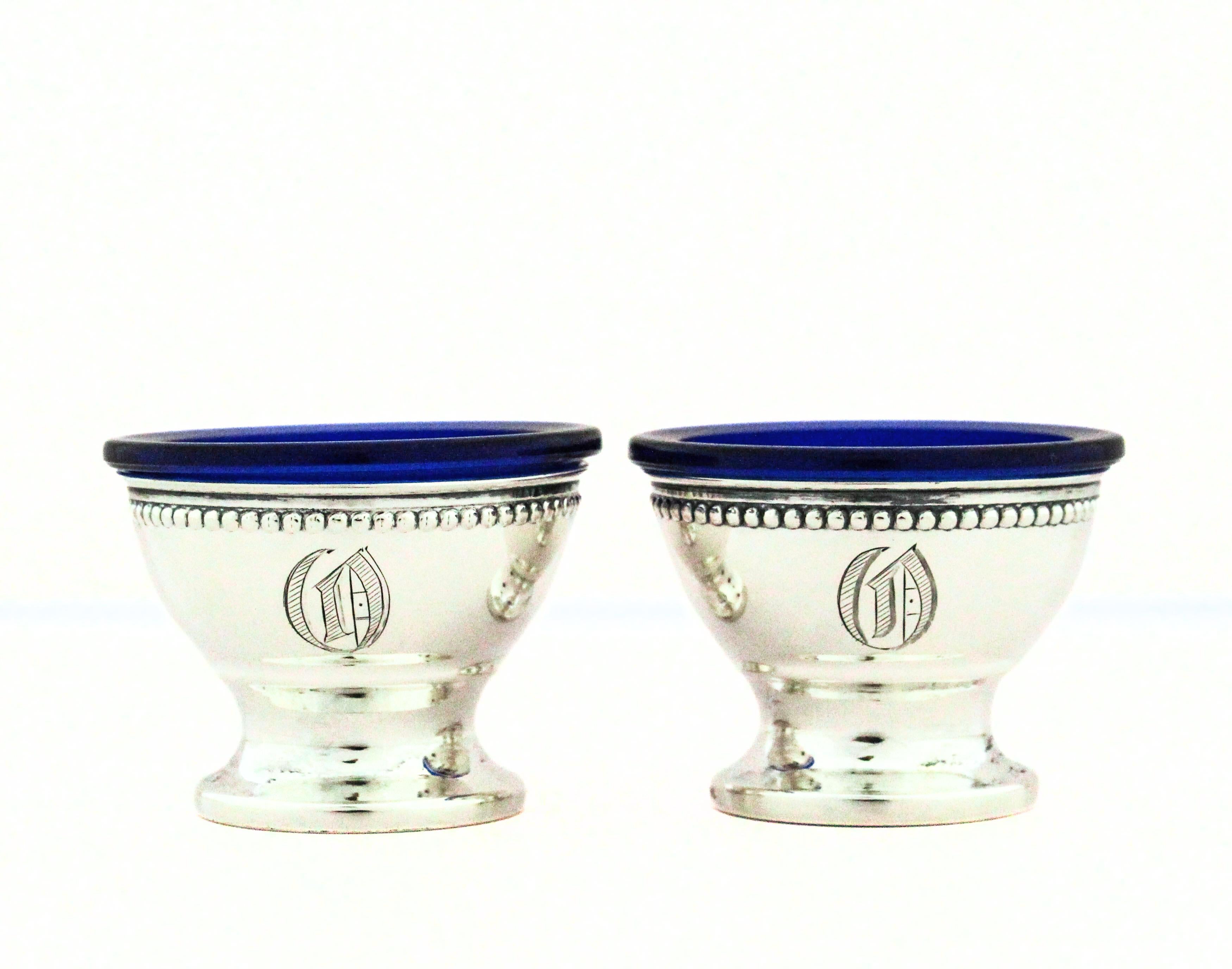 Un'elegante coppia di saliere in argento sterling, ciascuna meticolosamente realizzata in un'elegante forma classica. Le ciotole sono dotate di rivestimenti in vetro blu cobalto, perfettamente inseriti nelle cornici argentate per offrire protezione