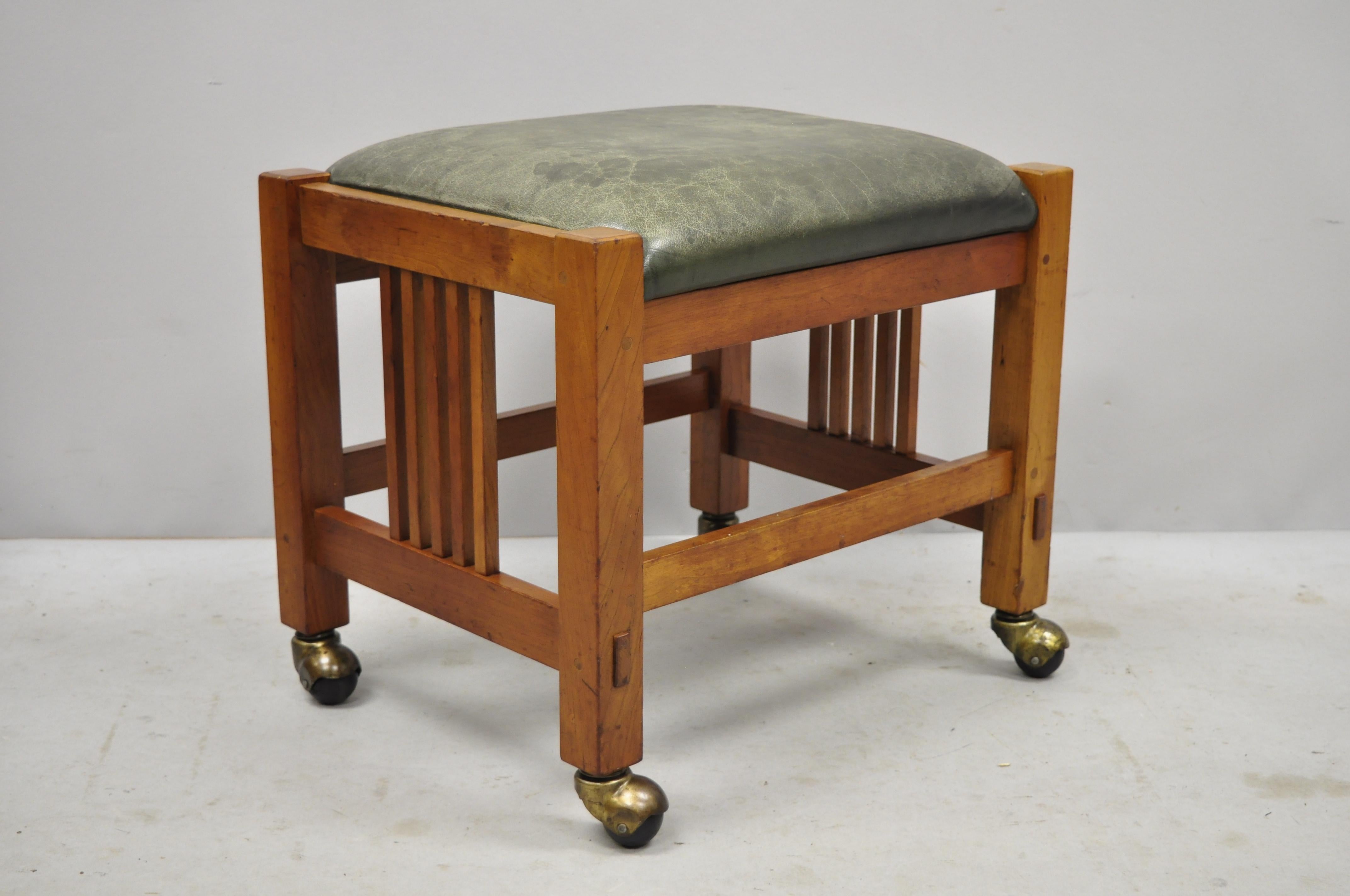 Pair of Stickley Mission Arts & Crafts cherrywood green leather ottoman stools. Listing includes rolling casters, solid wood construction, beautiful wood grain, distressed leather upholstery, original labels, quality American craftsmanship, circa