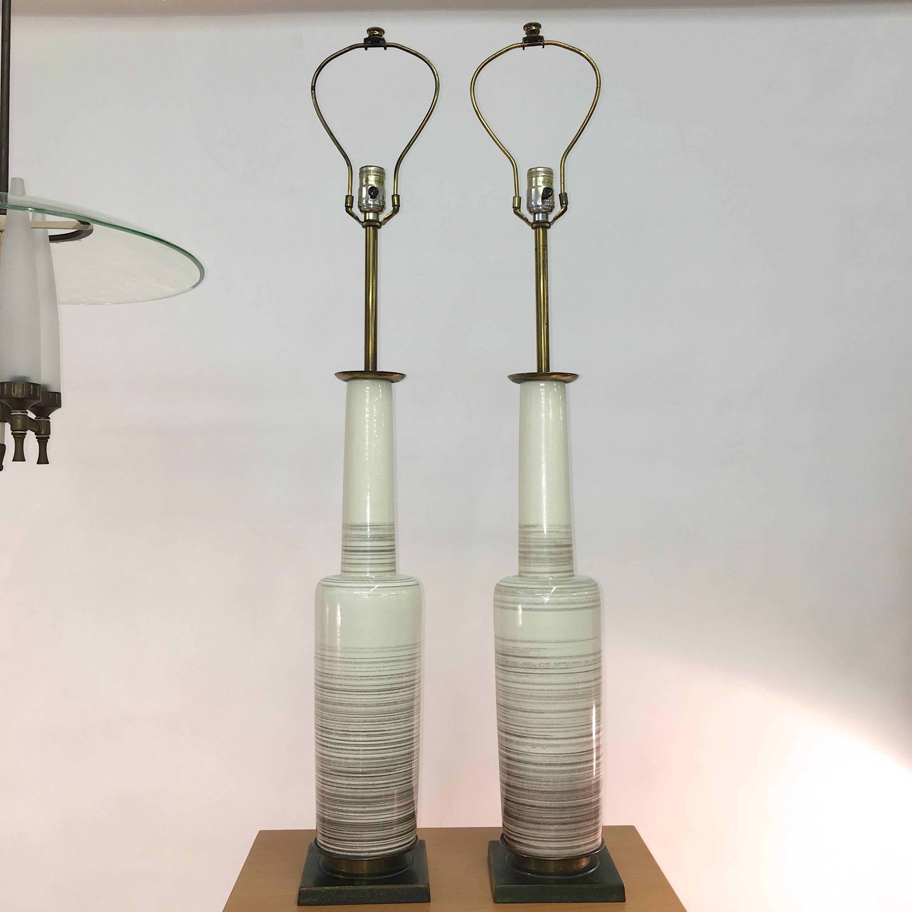 Pair of Mid-Century Modern glazed ceramic bottle vase form lamps on brass bases, in bone with charcoal brown striations and subtle craqueleur to glazing. 

Each measures 42in to top of finial 24in to top of base. Brass bases are 6 inches square and