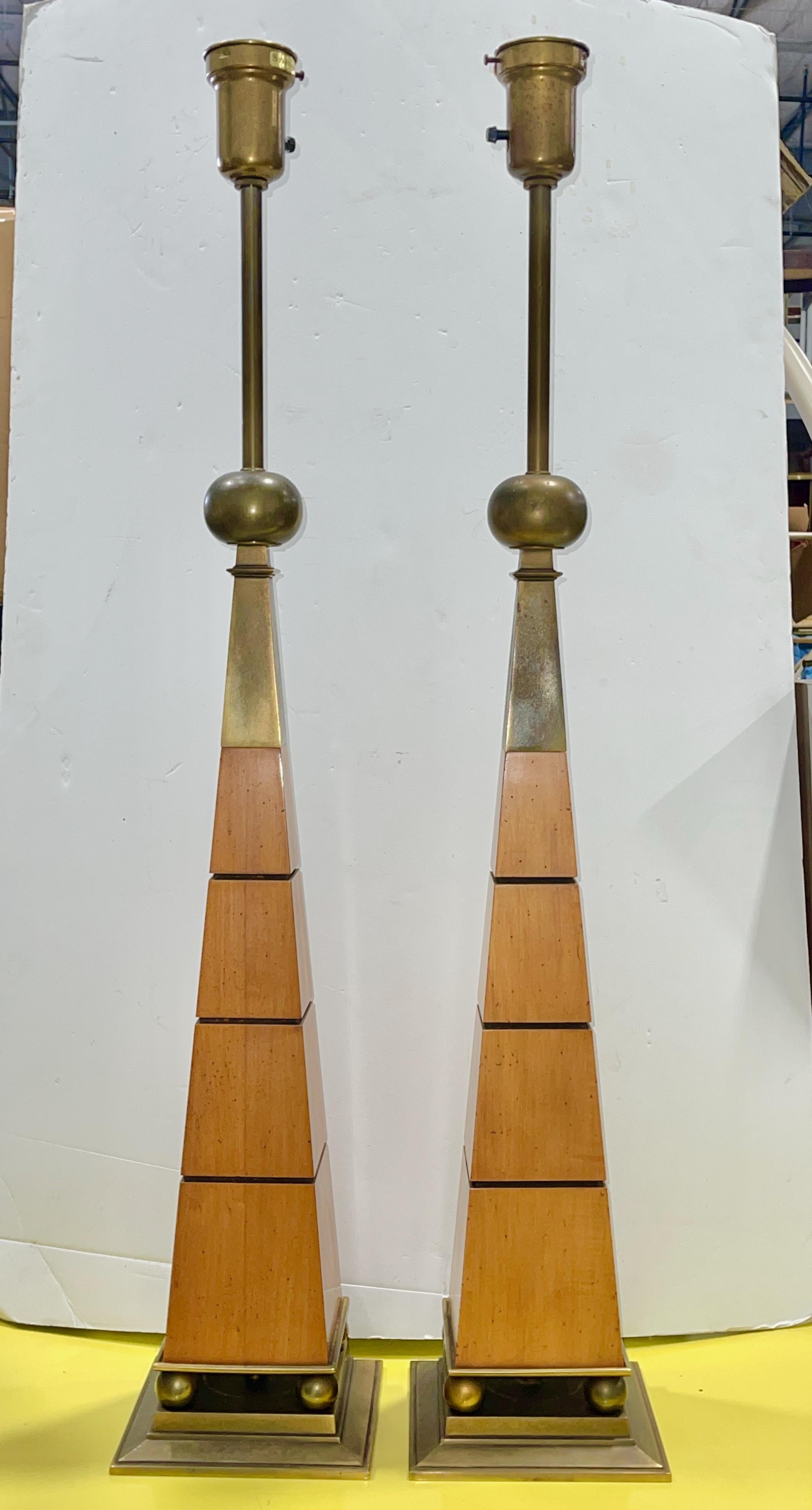 Impressively tall and architecturally inspired pair of vintage 1960's table lamps in the style of Tommi Parzinger in pecan wood and bronze-tone brass.
Four spheres atop a plinth base support an tapering obelisk-form body with horizontal dadoed