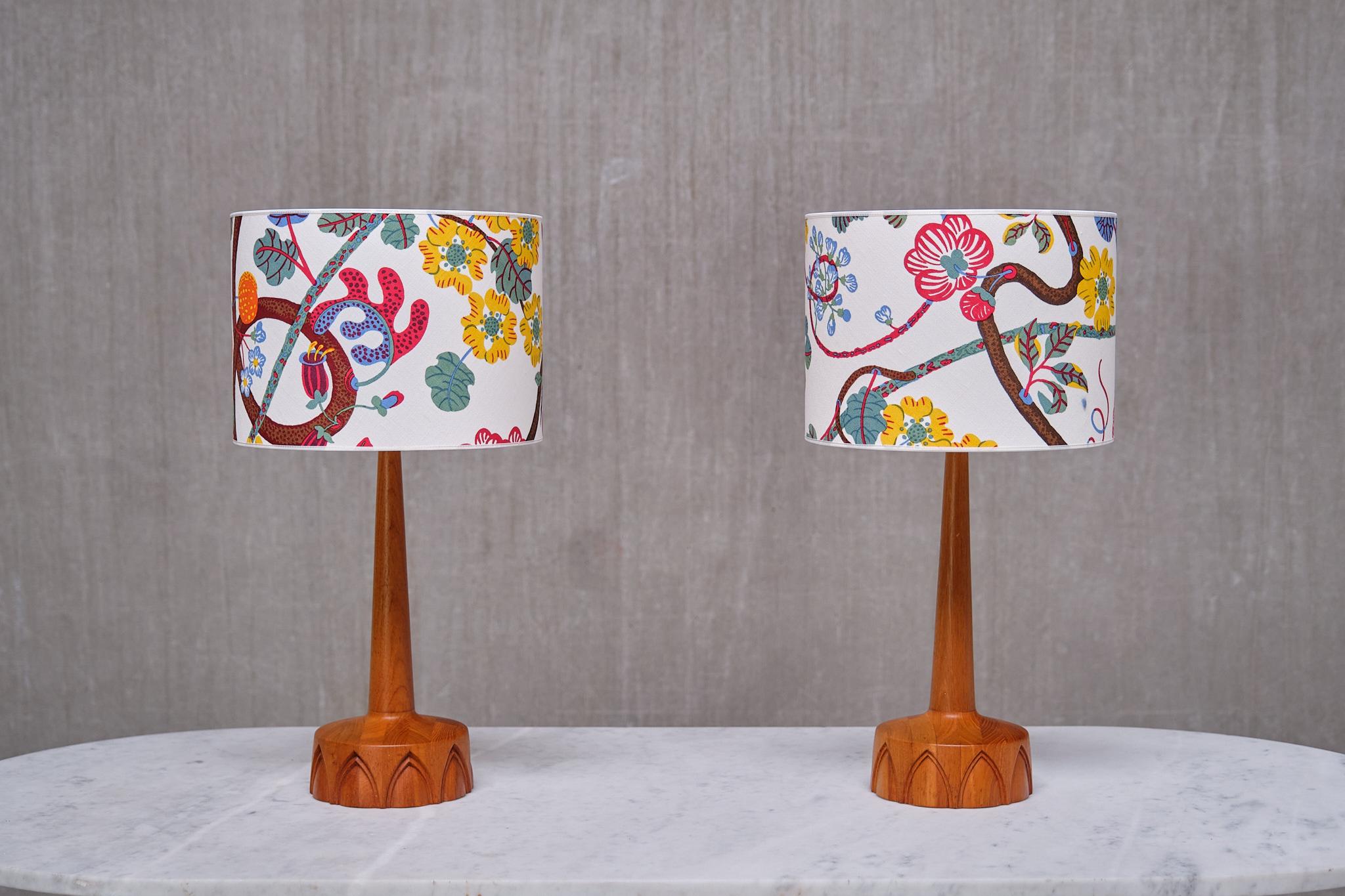 Cette élégante paire de lampes de table a été produite par AB Stilarmatur Tranås en Suède dans les années 1960. Fabriquées en bois de teck, les bases circulaires sont ornées d'un intéressant motif arqué sculpté à la main. Tige conique et magnifique