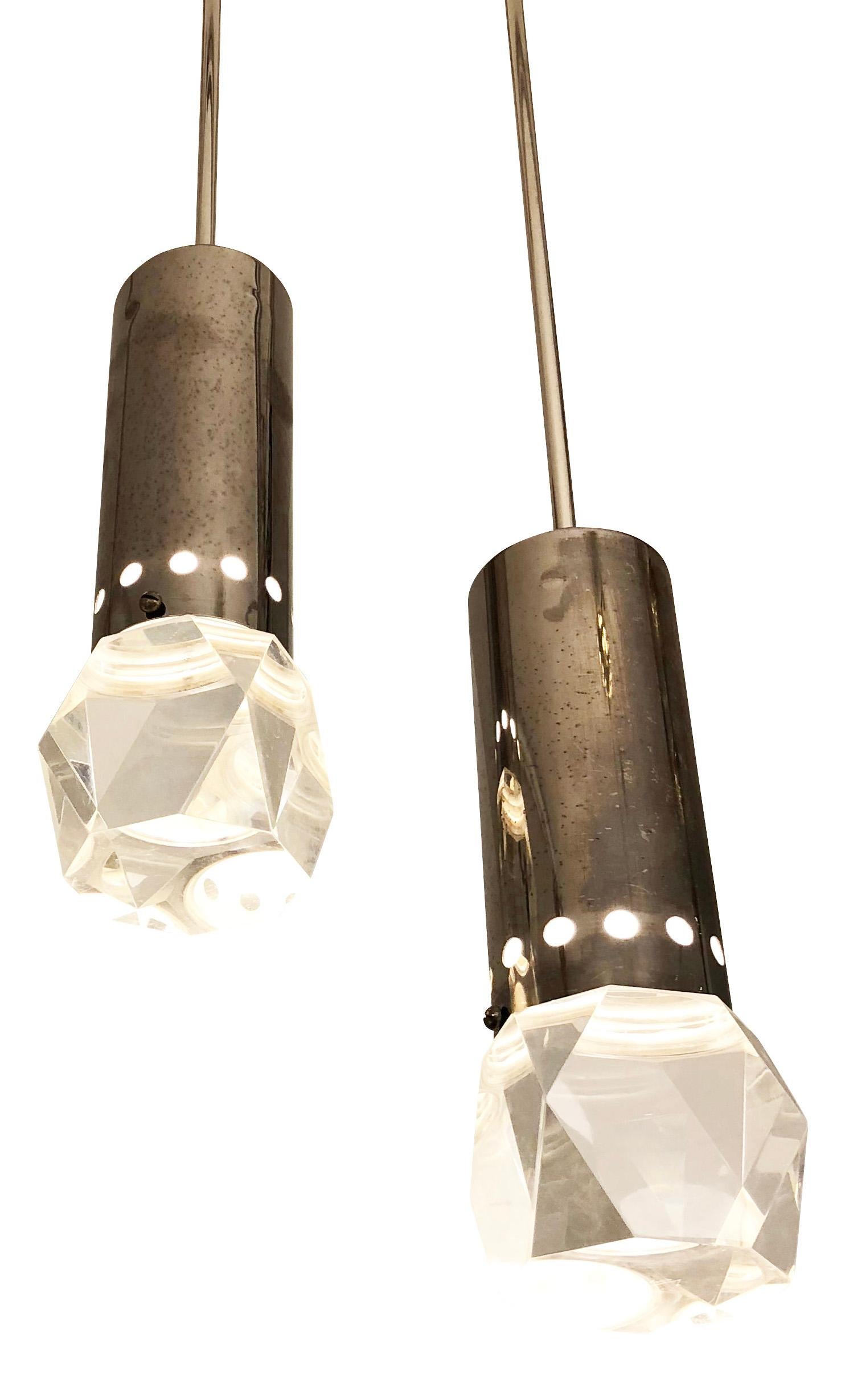Midcentury pendants by Stilnovo with faceted Lucite shades. The many facets create beautiful light reflections that change as you move around them. Cylindrical hardware is perforated and finished in a dark nickel patina. Can be mounted together on